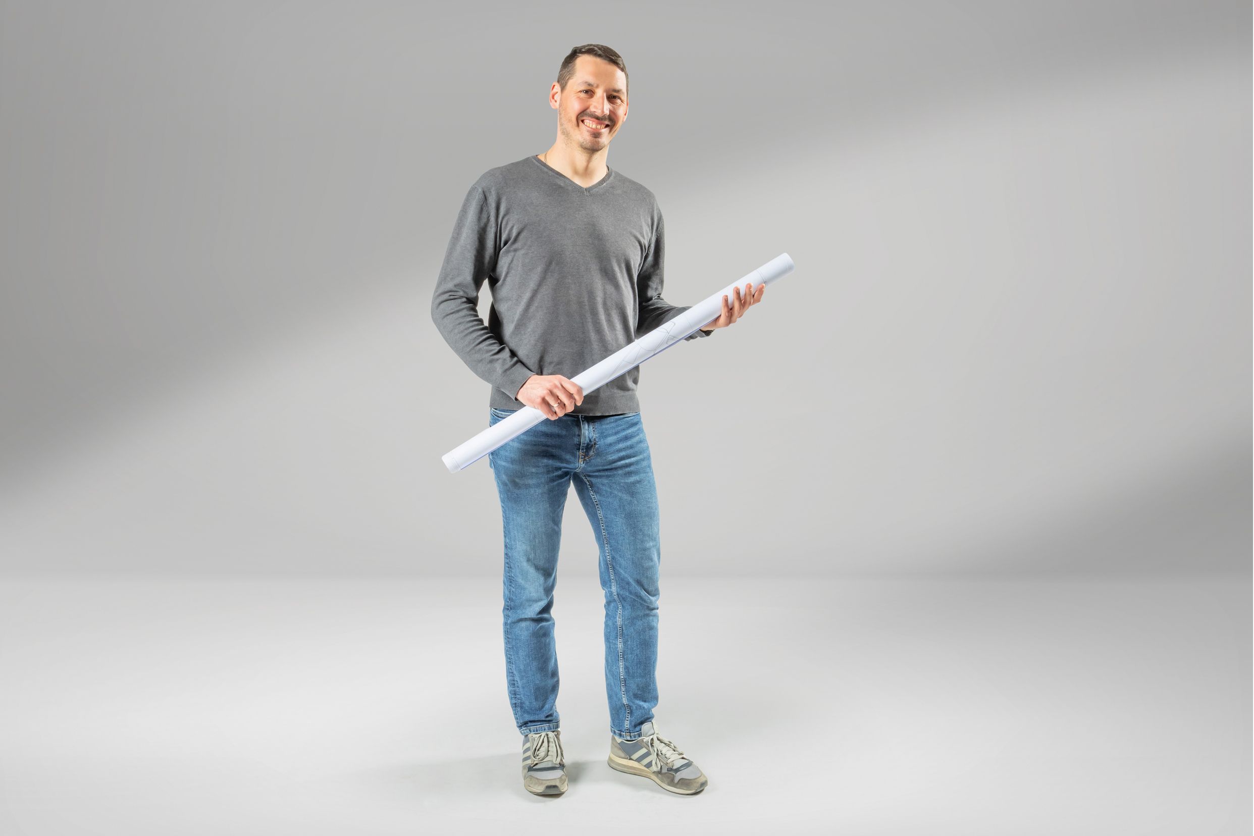 Ein Mann mit einem aufgerollten Plan in der Hand lacht freundlich in die Kamera.