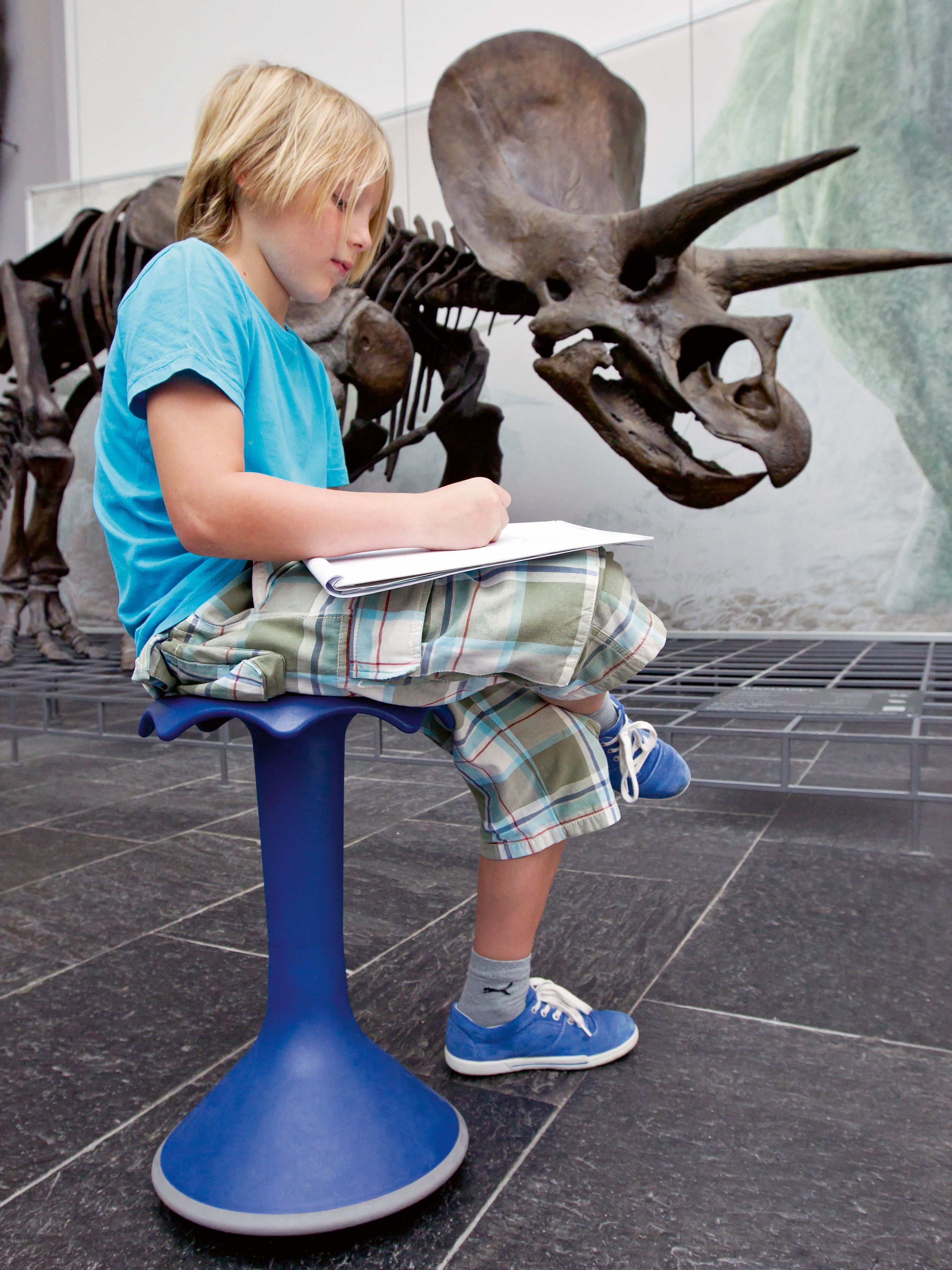 A boy draws sitting on a blue Hokki made by VS in the Senckenberg Natural History Museum in Frankfurt