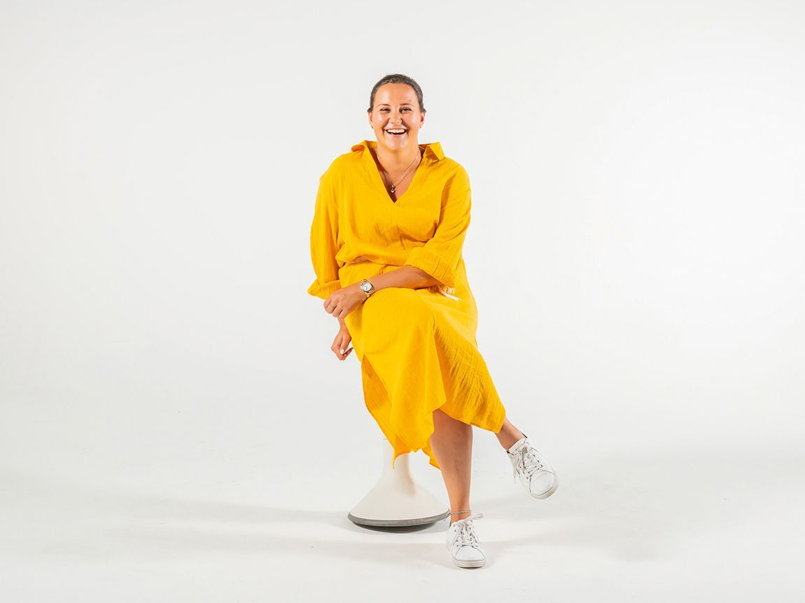 Young woman in a yellow dress sits on the ergonomic stool Hokki by VS