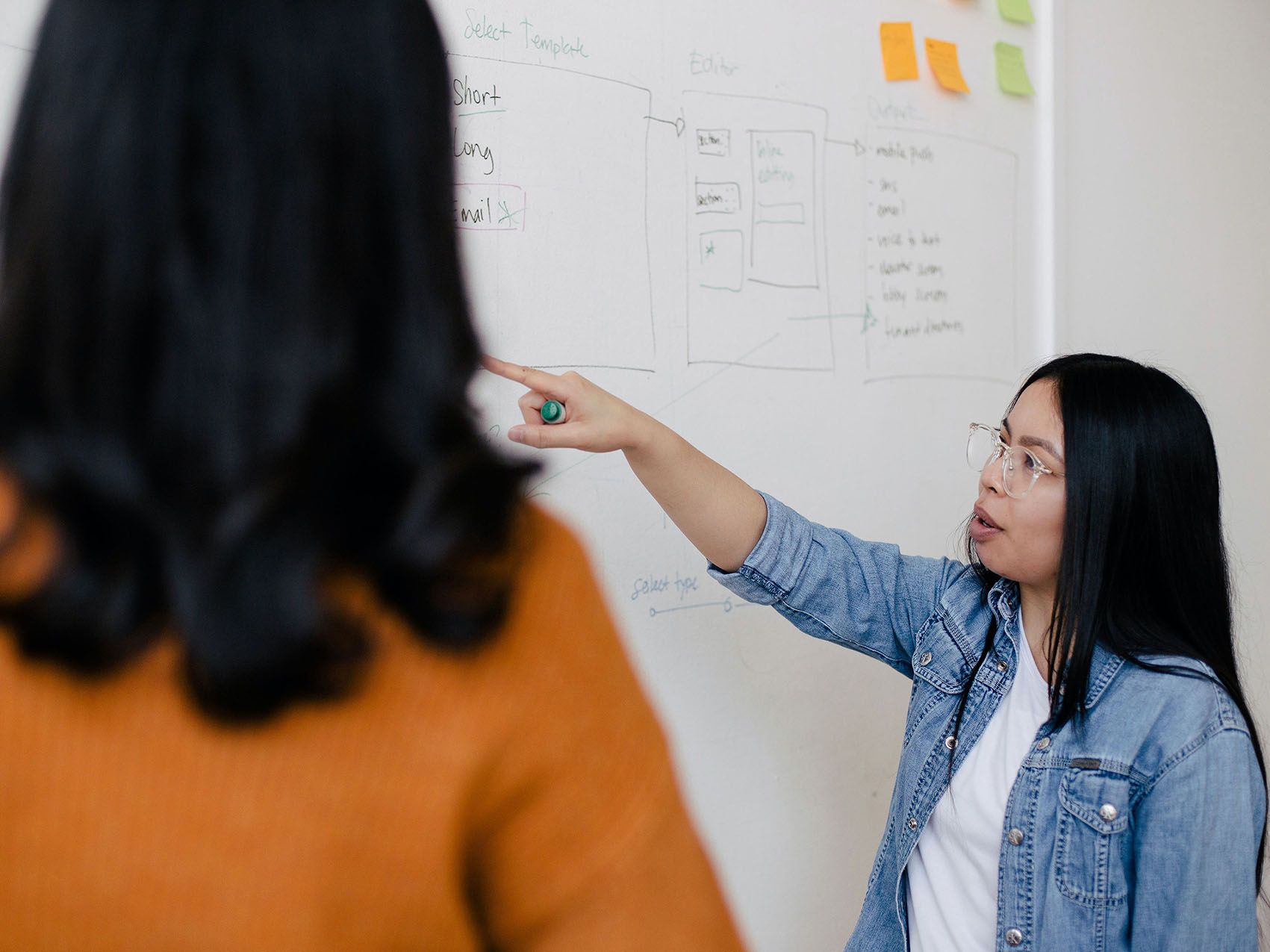 Deux femmes discutent devant un tableau blanc