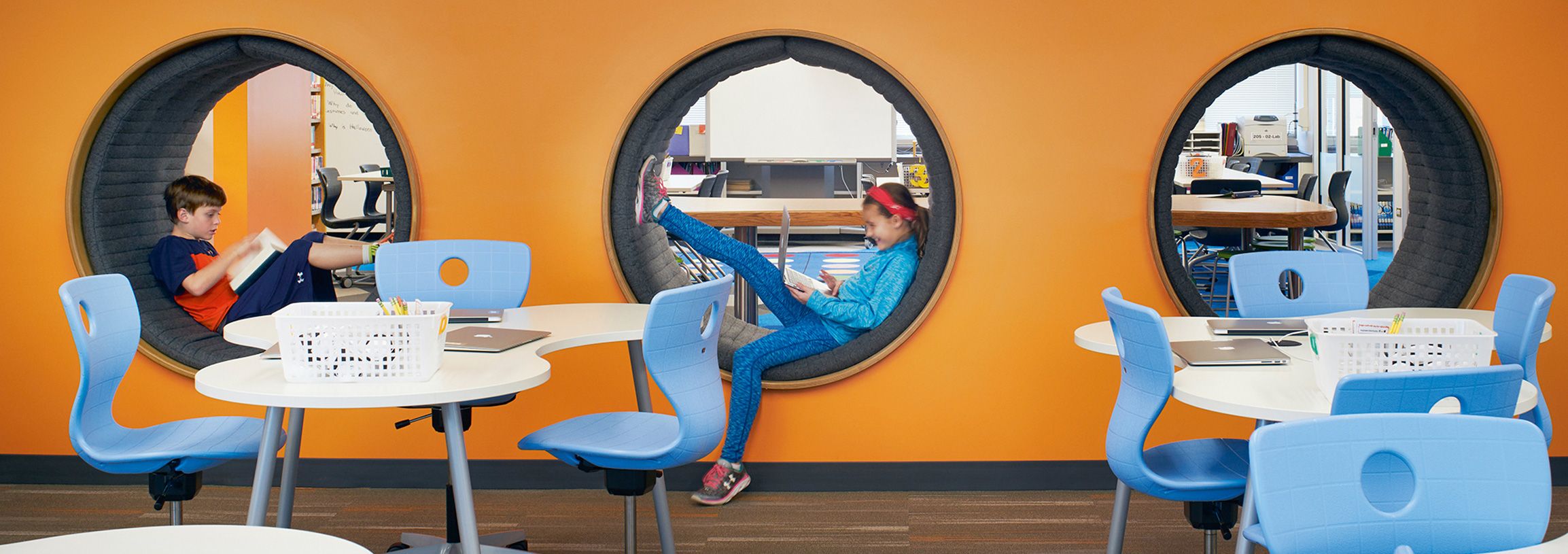 Round, padded holes in a wall serve as a reading retreat for two children