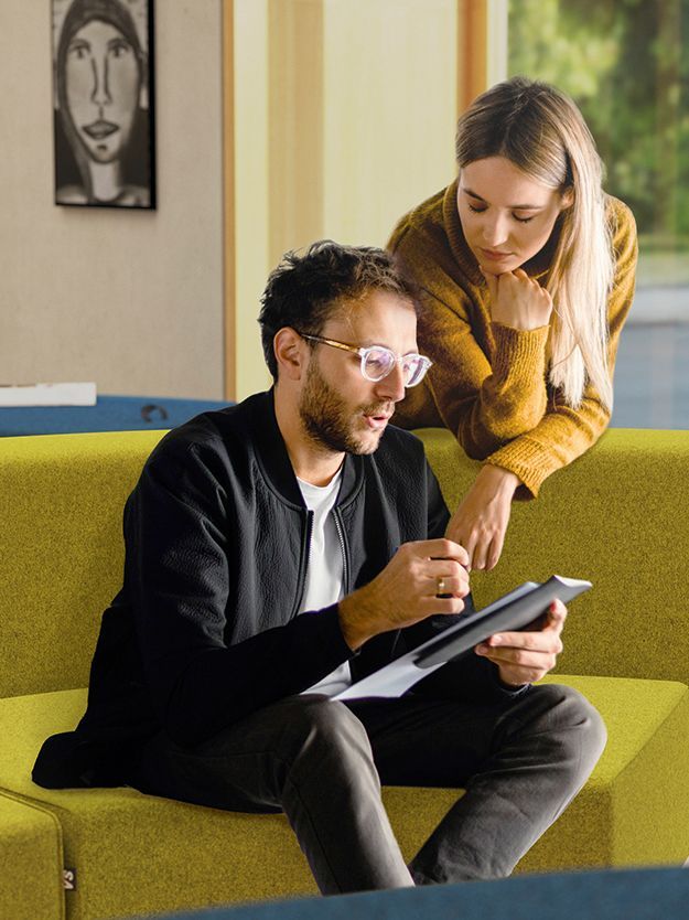 A man sits on the LowBack sofa from the Lounge series by VS and discusses something with a woman leaning on the backrest