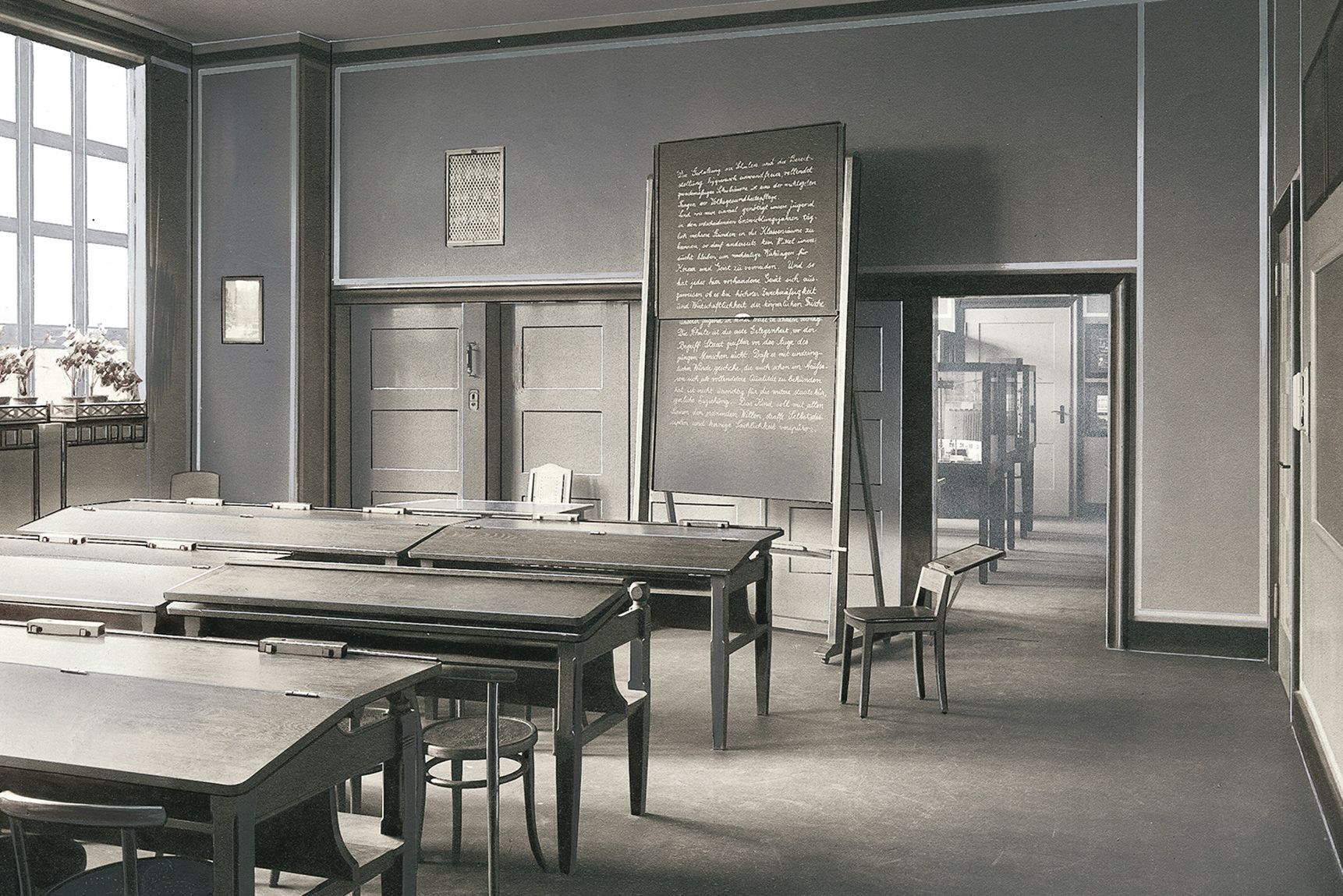 Black and white picture of a typical classroom from 1910 with a slate blackboard and old school desks