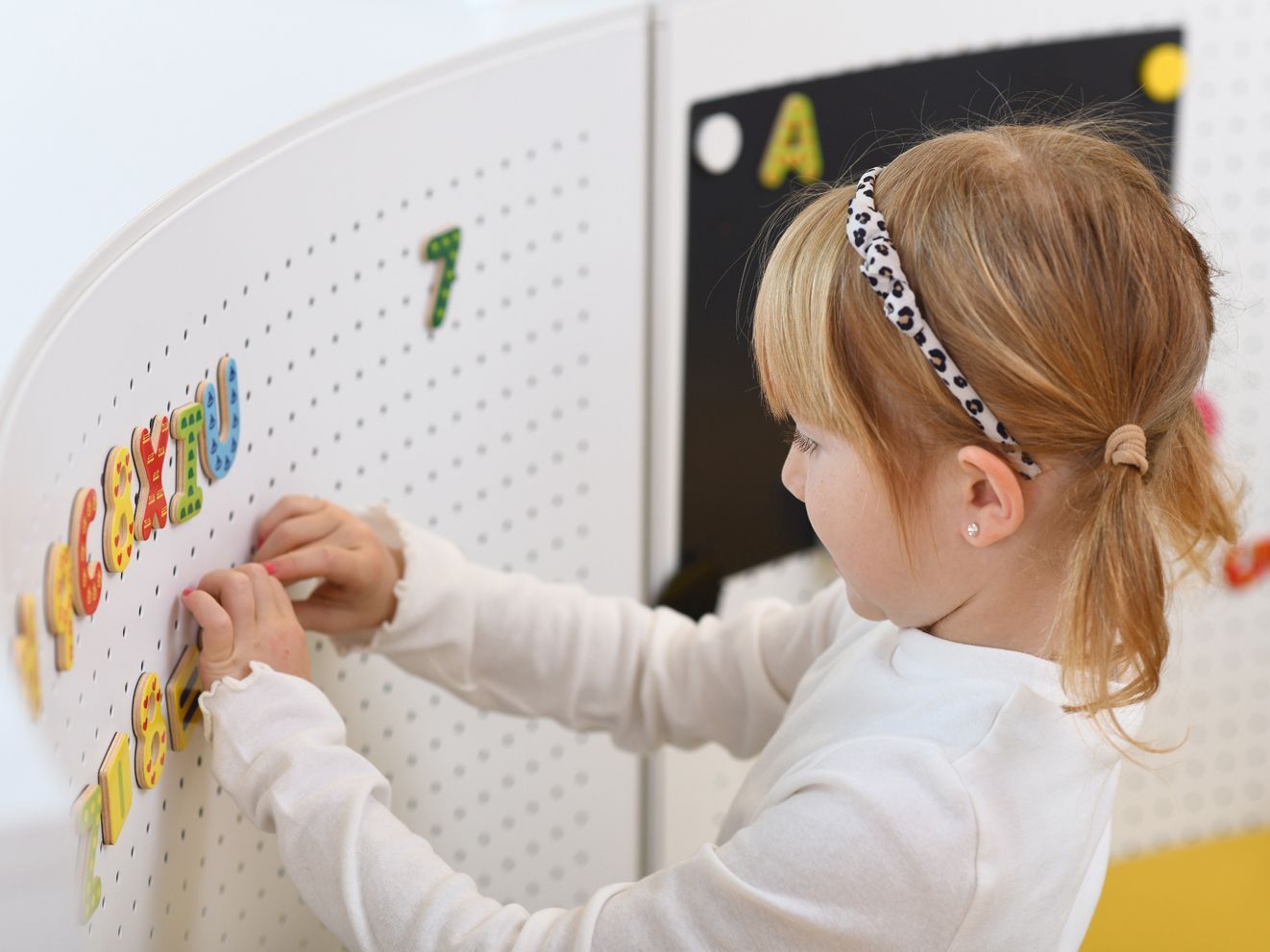 A girl learns with magnetic letters and digits on a perforated partition screen.