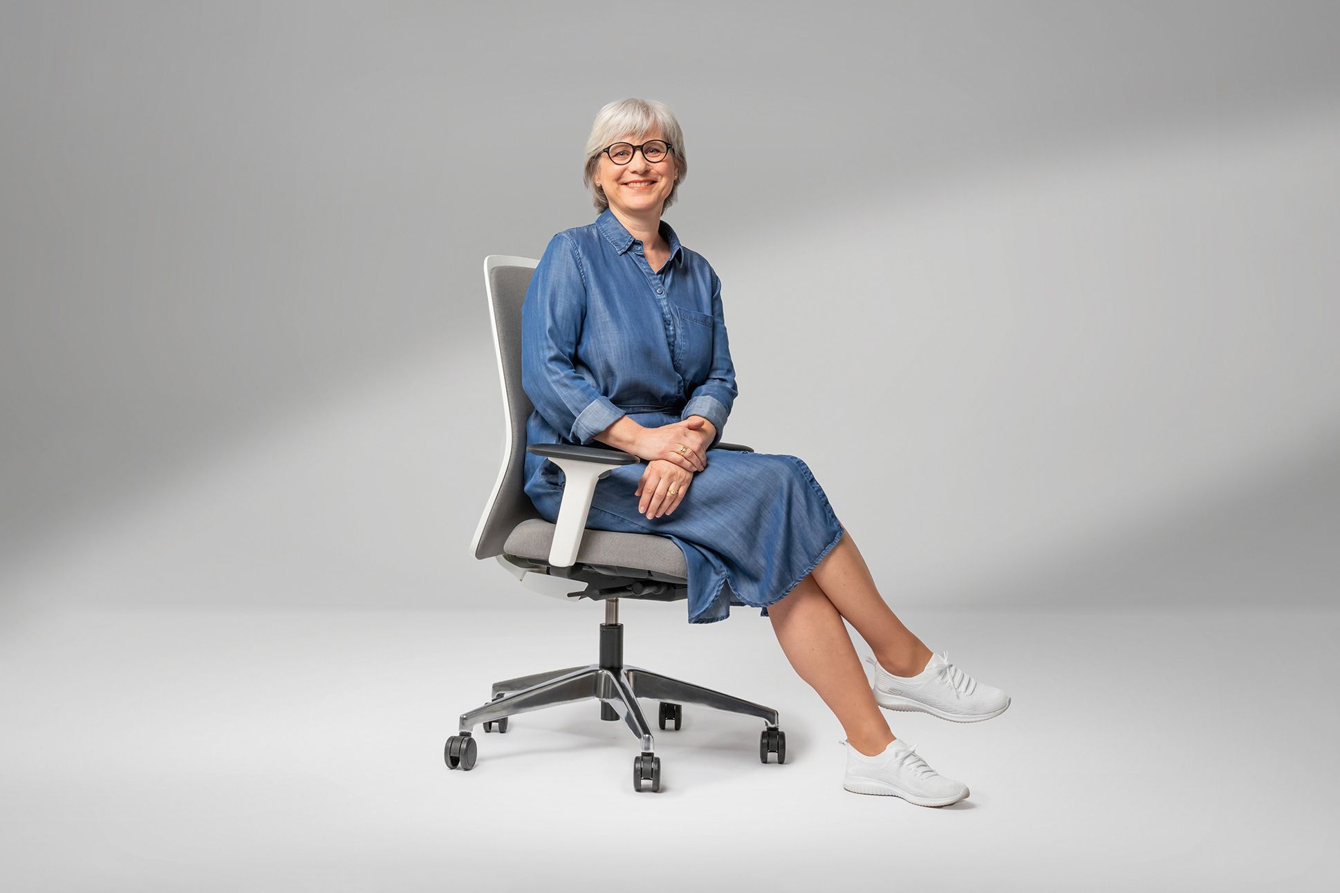 woman sitting on a grey, upholstered office swivel chair with armrests and castors