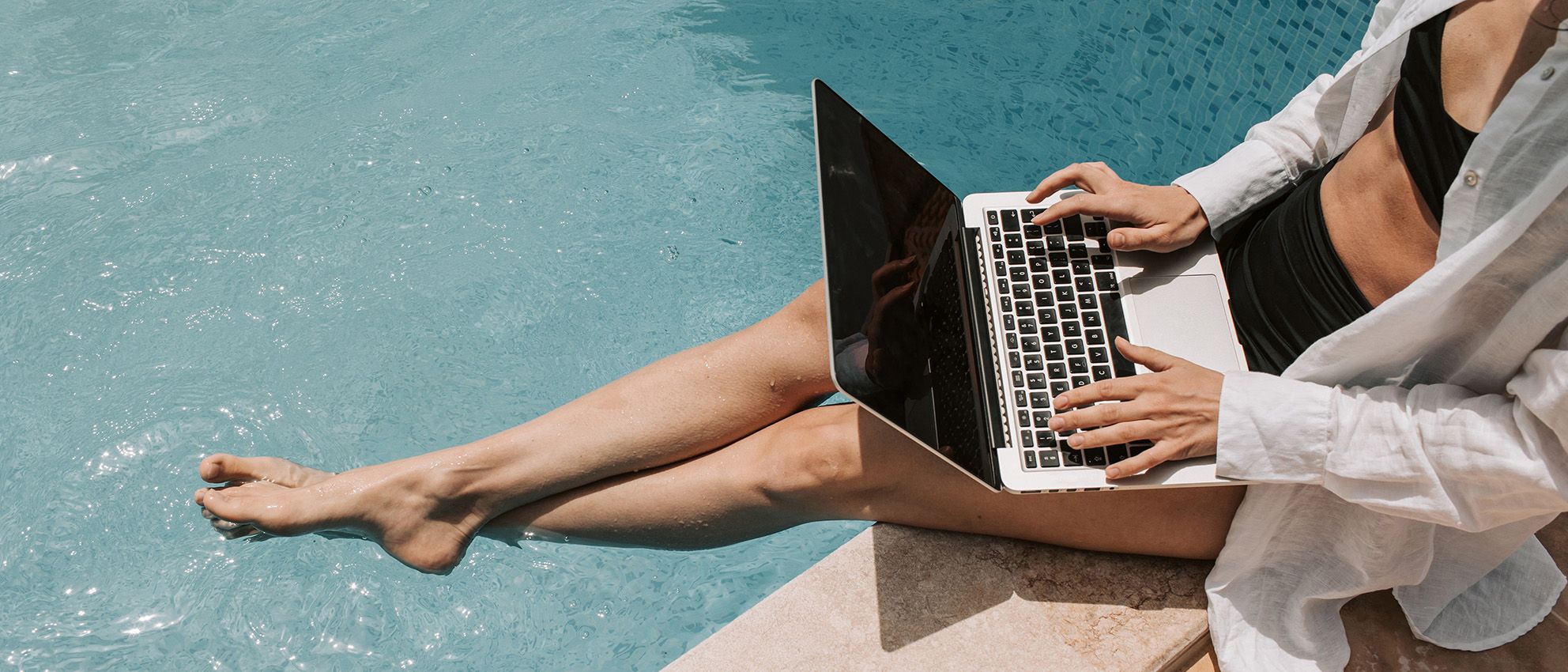 Ausschnitt einer Person, die mit einem Arbeitslaptop am Pool sitzt.