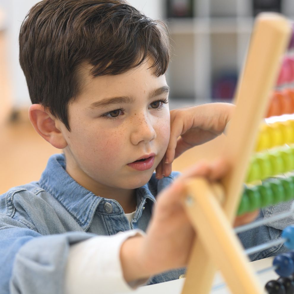 A boy learns arithmetics with an abacus on floor-level furniture from the FloorFriends series by VS.