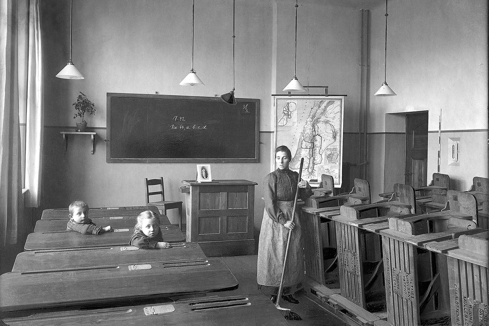 Eine Frau kehrt neben hochgeklappten Rettig-Bänken in einem Klassenzimmer