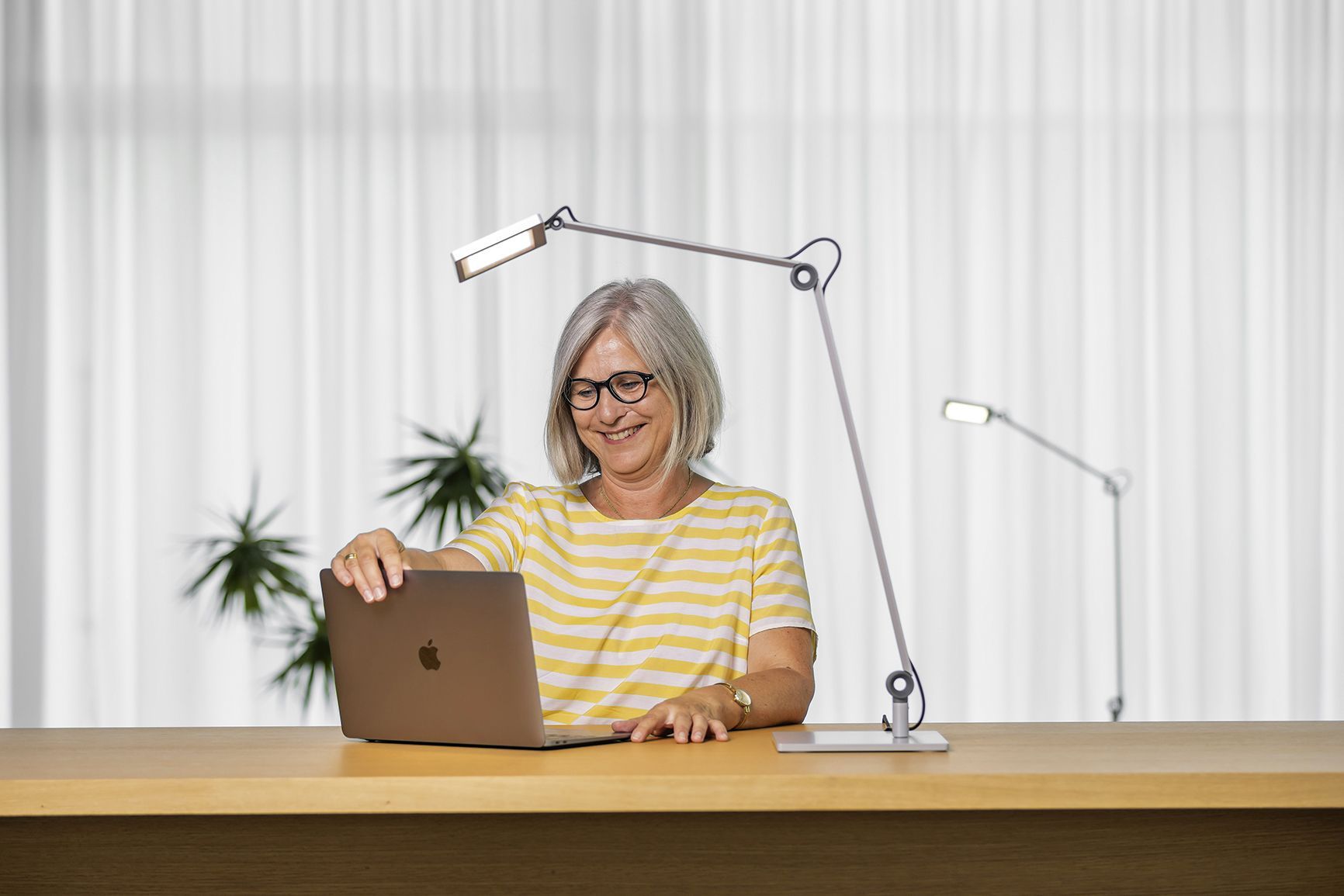 A woman works on a laptop next to the PARA.MI desk lamp