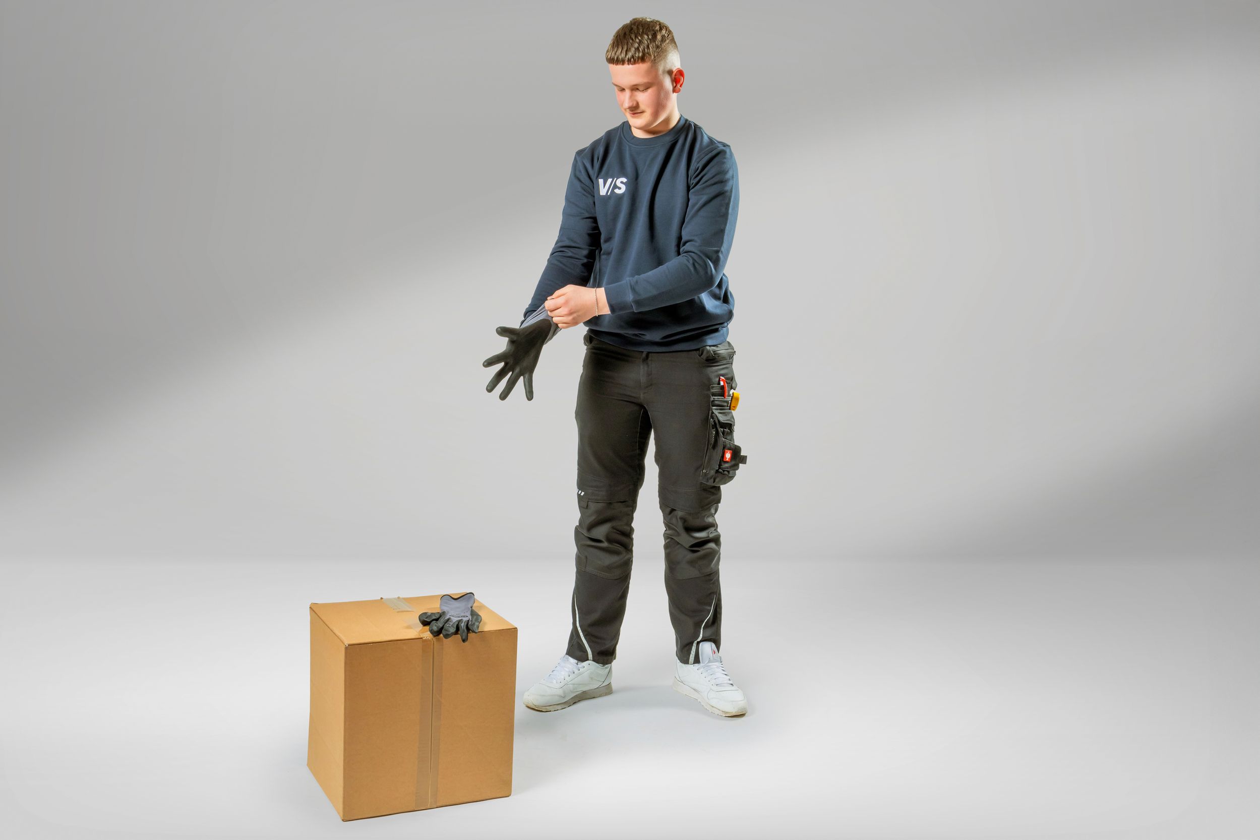 Ein Teenager, der eine Ausbildung zum Lagerlogistiker macht und sich gerade die Handschuhe anzieht.