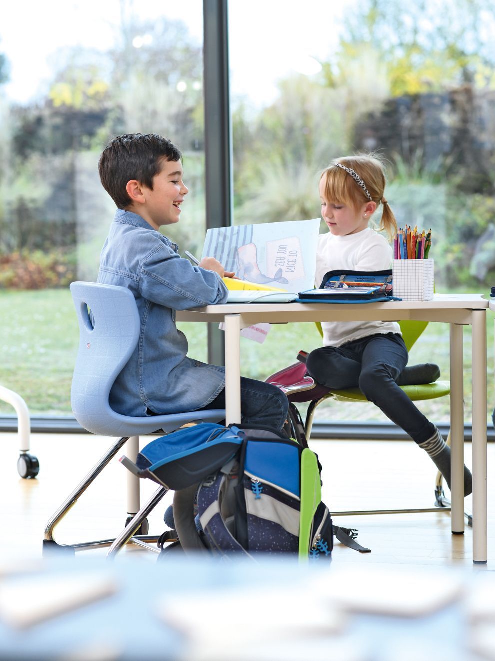 Two children sit together at the table on PantoSwing students' chairs by VS and draw pictures.