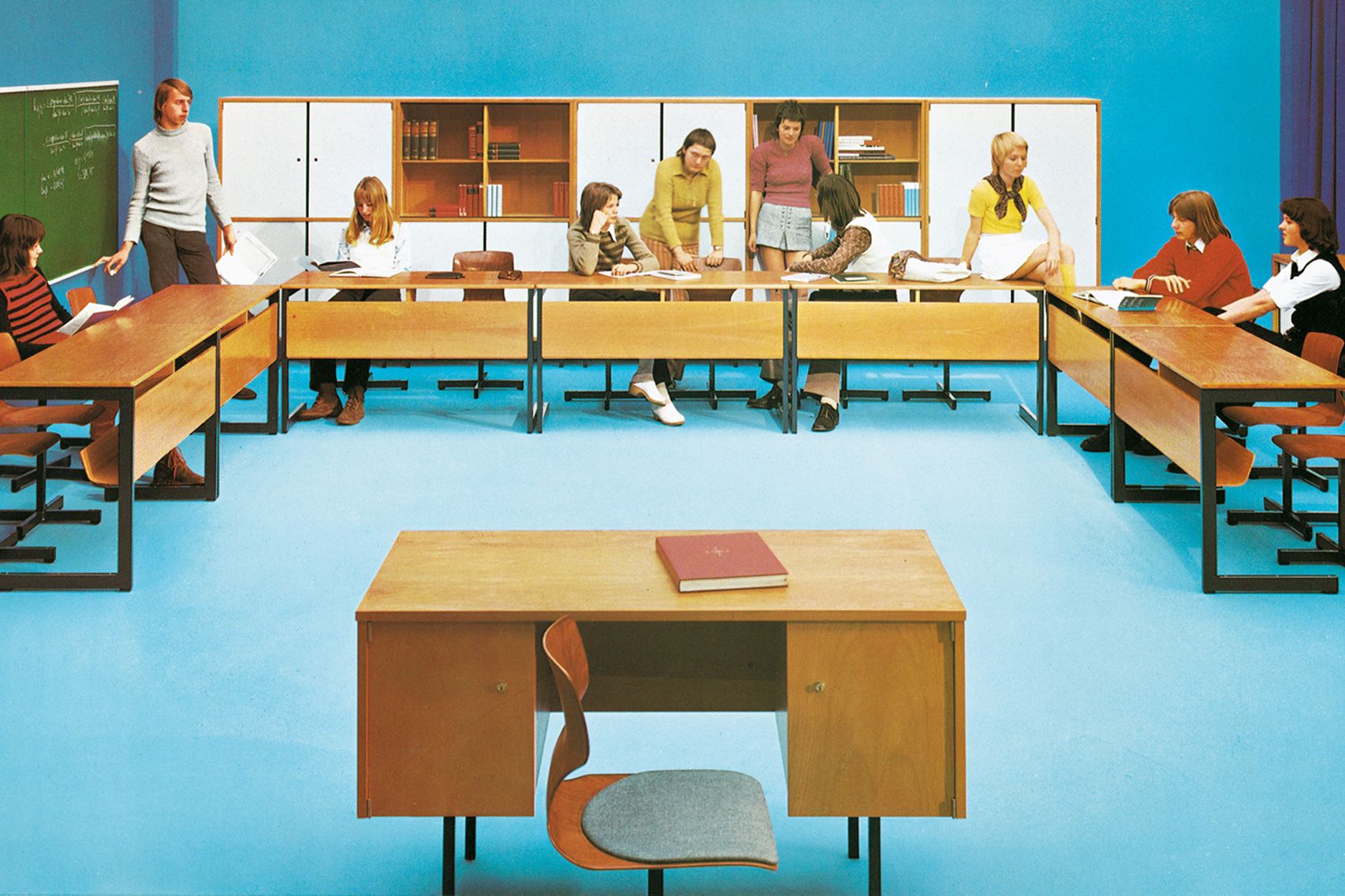 Classroom from the sixties where students are learning, sitting and standing at desks