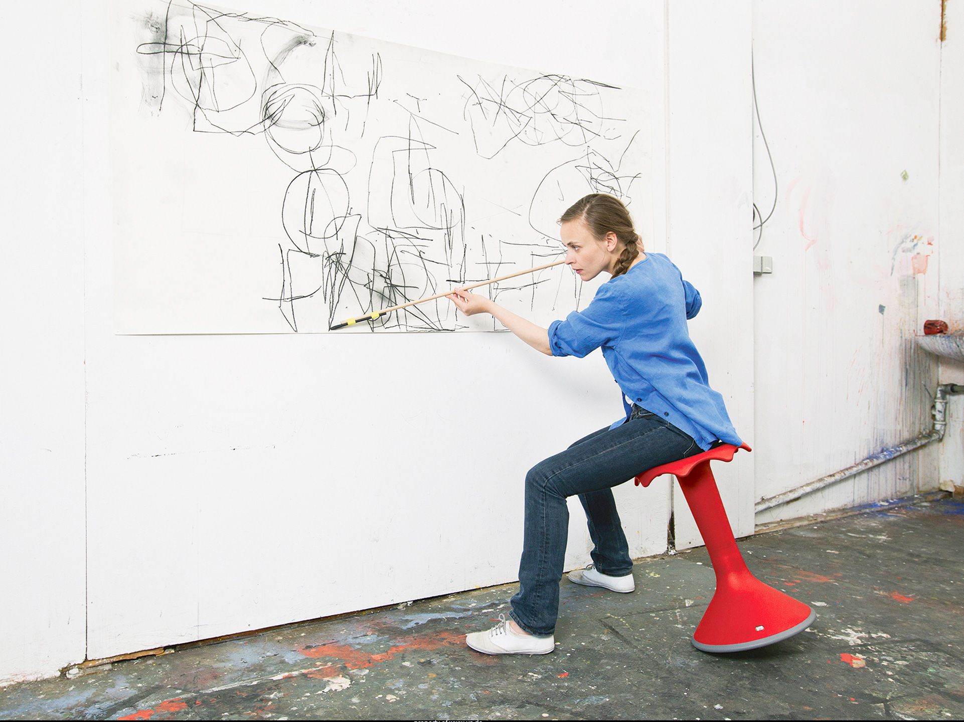 An artist sits on a red Hokki and paints a painting