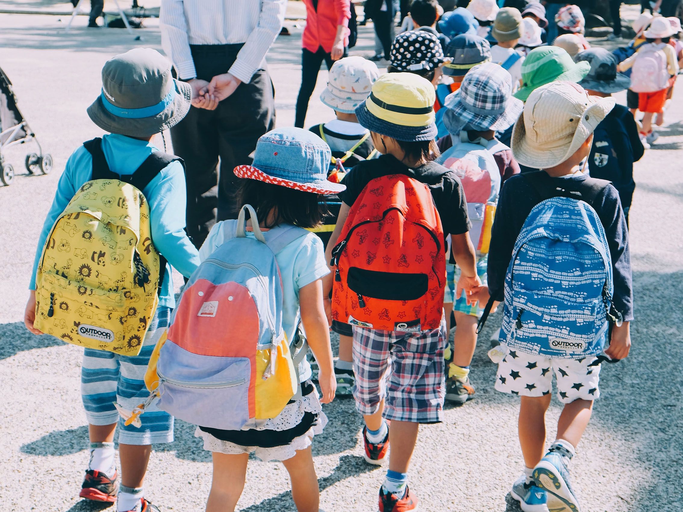 Lors d'une sortie, plusieurs enfants marchent en file avec leur sac à dos d'écolier.