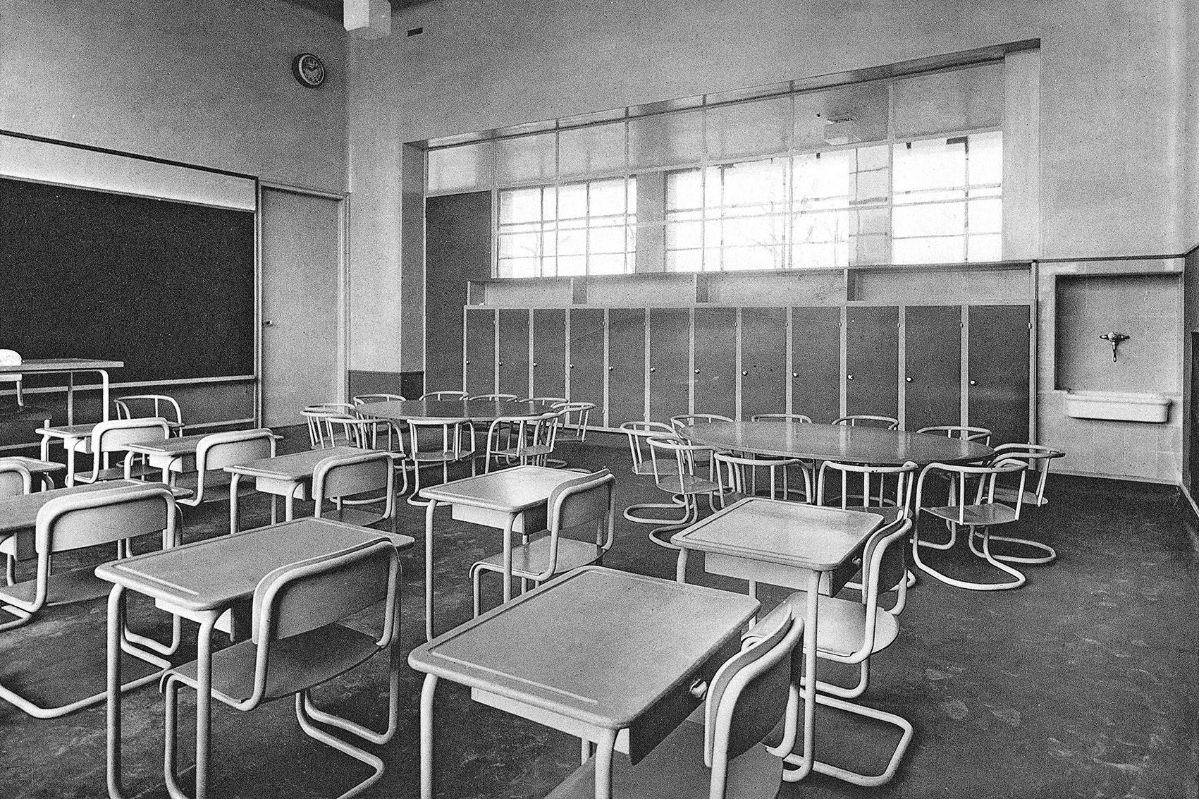 Black and white picture of a classroom from 1930 with chairs and tables made of tubular steel and a slate blackboard