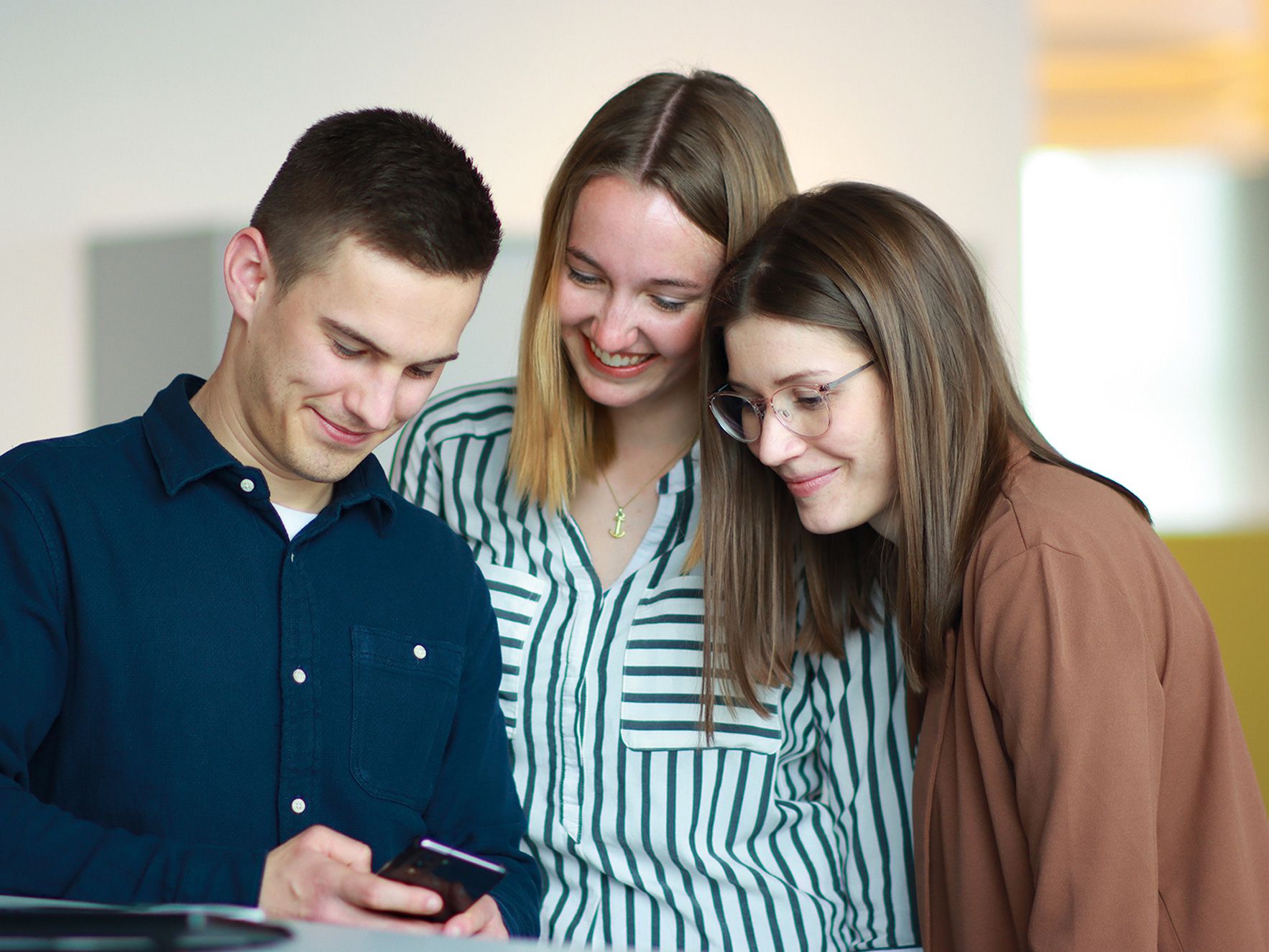 Three apprentices are spending time together laughing about something funny on a smartphone.