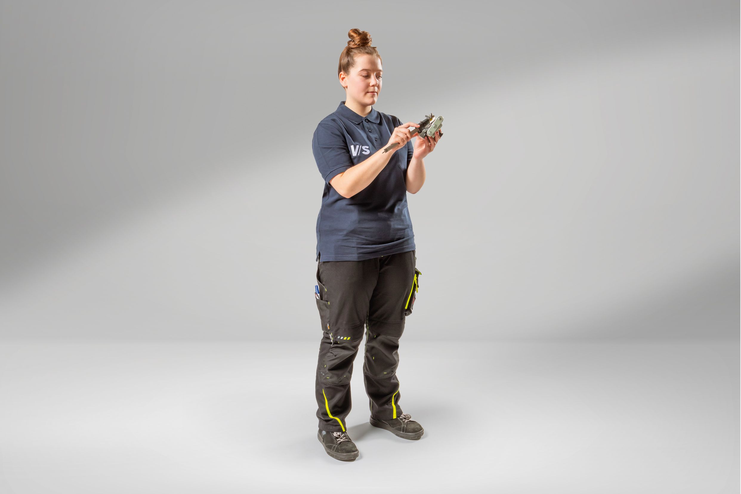 Young woman training as an industrial mechanic measures an object.