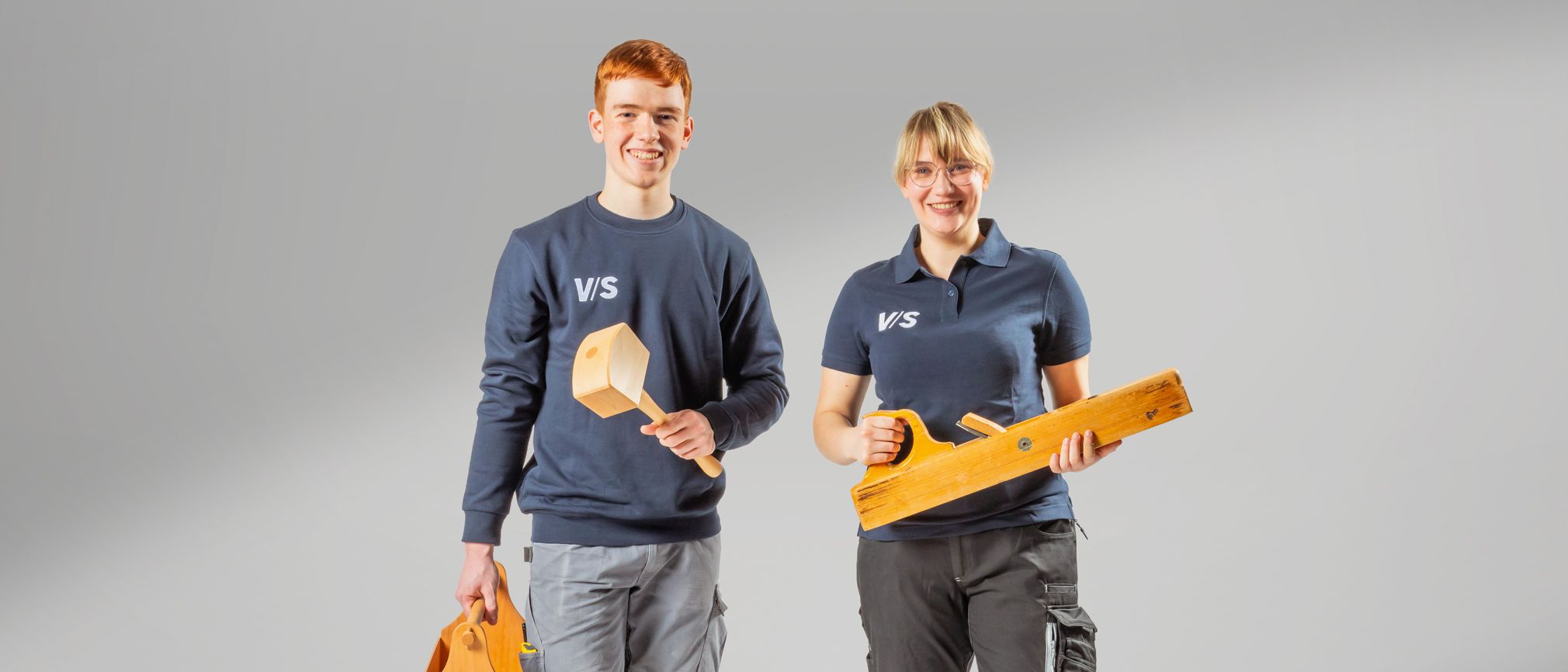Zwei jugendliche Auszubildende von VS mit Holzwerkzeug in der Hand.