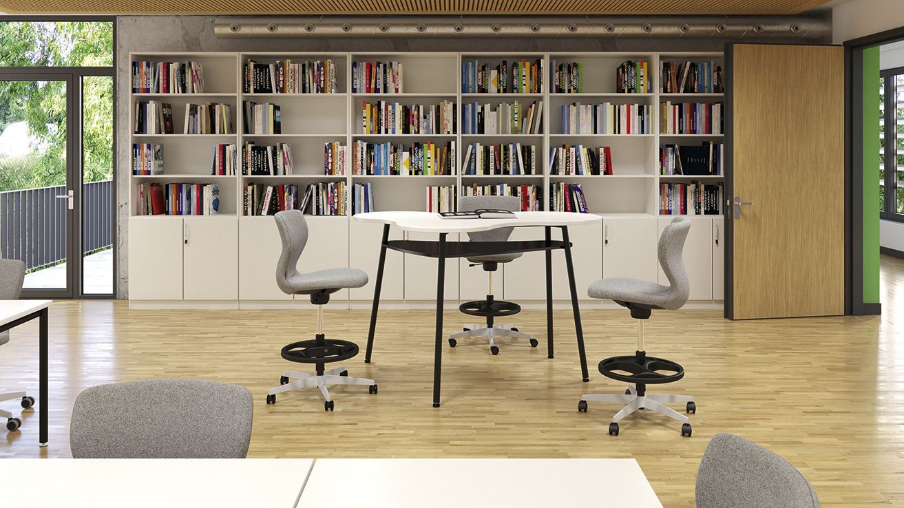 A VS TeamTable bar table with upholstered PantoMove-Soft chairs by VS in front of a wall of bookshelves