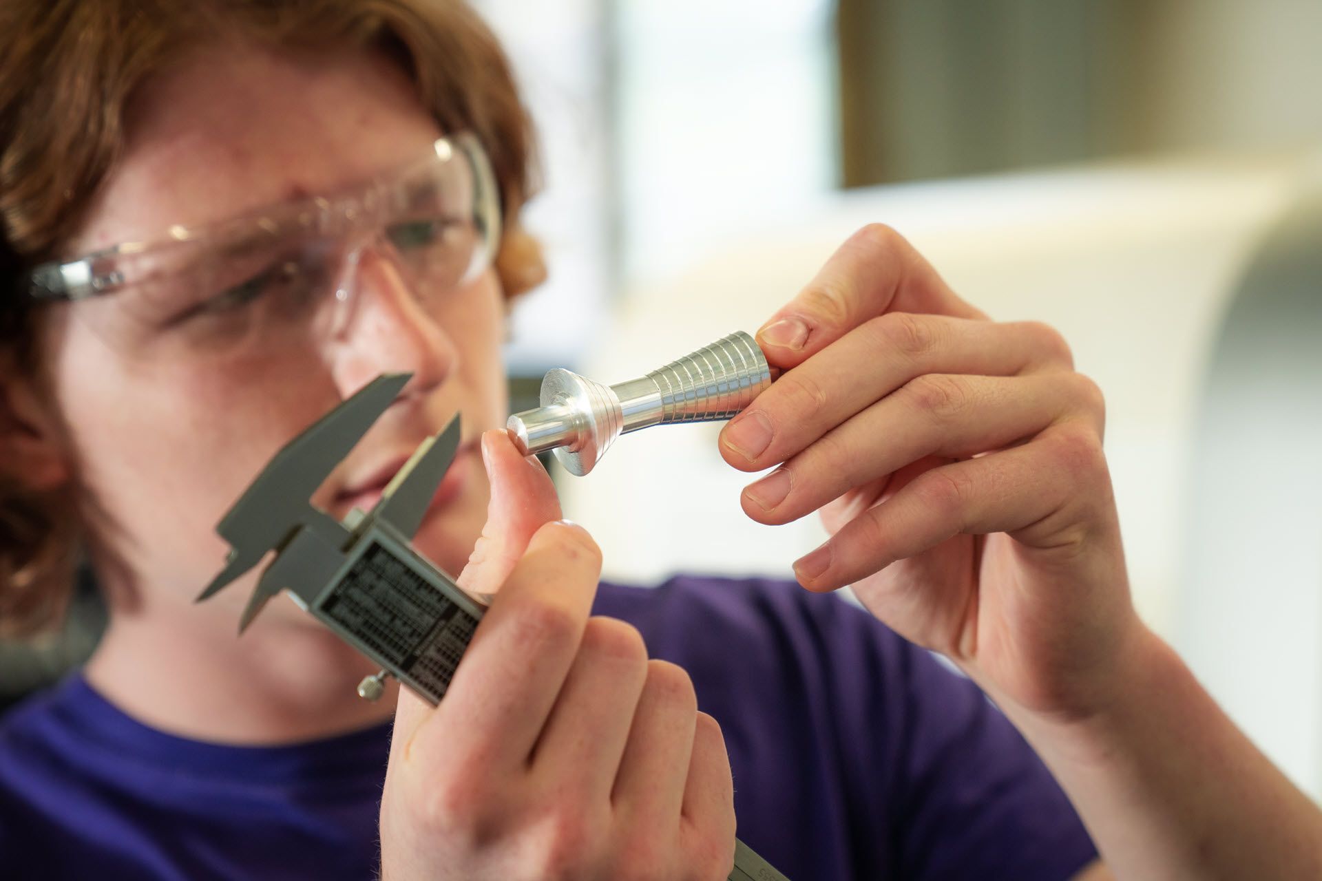 A young apprentice examines a small metal part with a calliper.