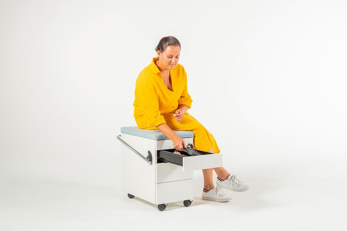 Young woman in a yellow dress sits on the OfficeBox mobile filing cabinet by VS and reaches into the drawer.