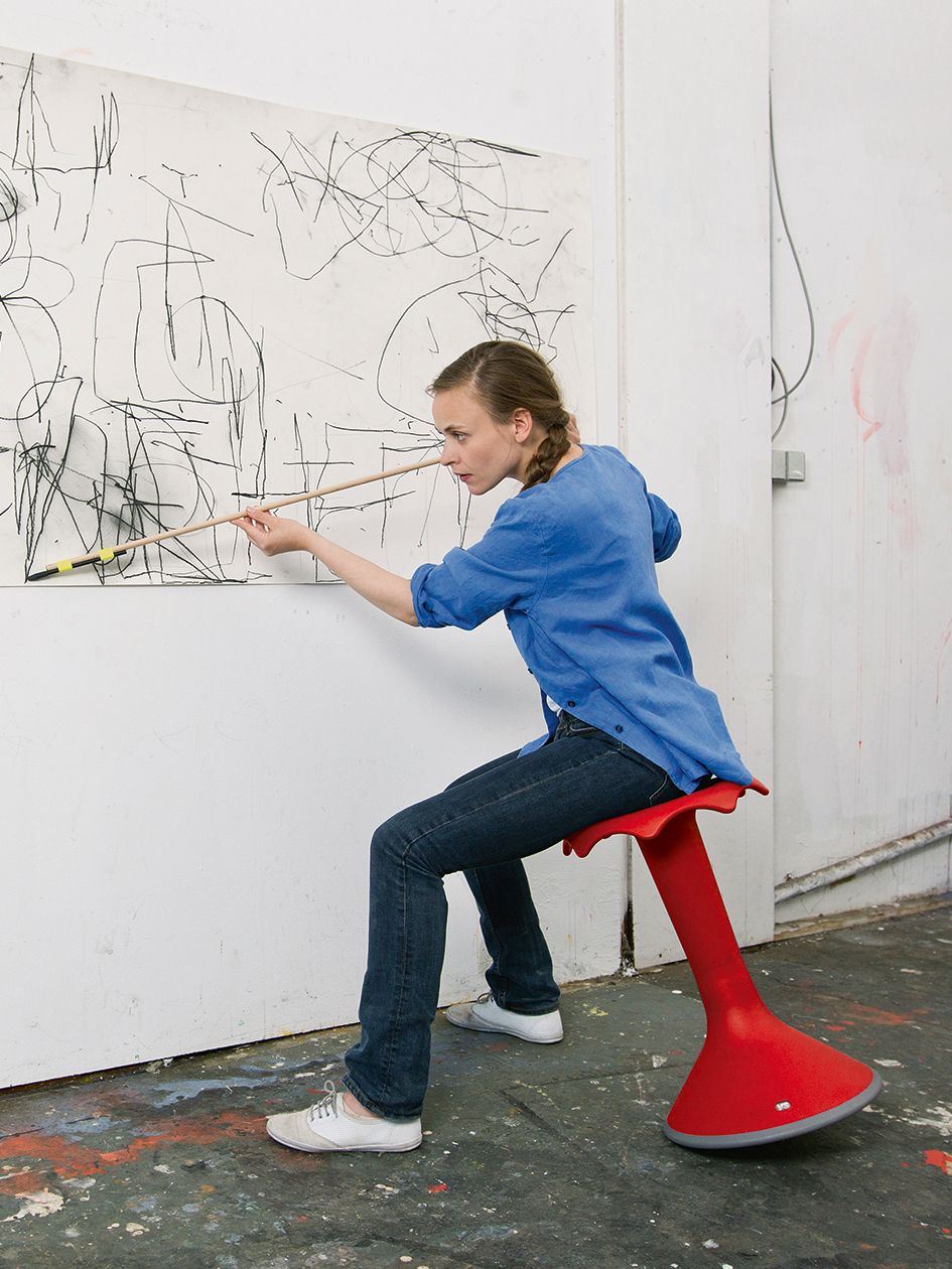 An artist sits on a red Hokki and paints a painting