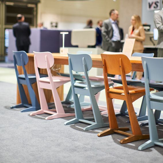 Holzkufenstühle von VS in Pastellfarben auf einer Messe-Ausstellung.