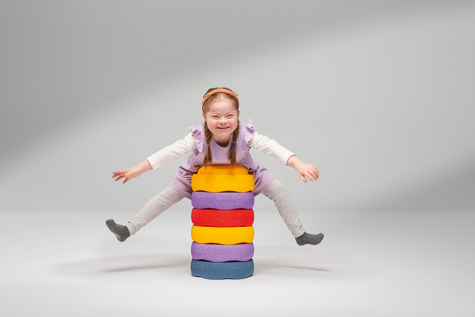 A girl is lying on her stomach on a stack of Stapelstein stones from the FloorFriends series by VS