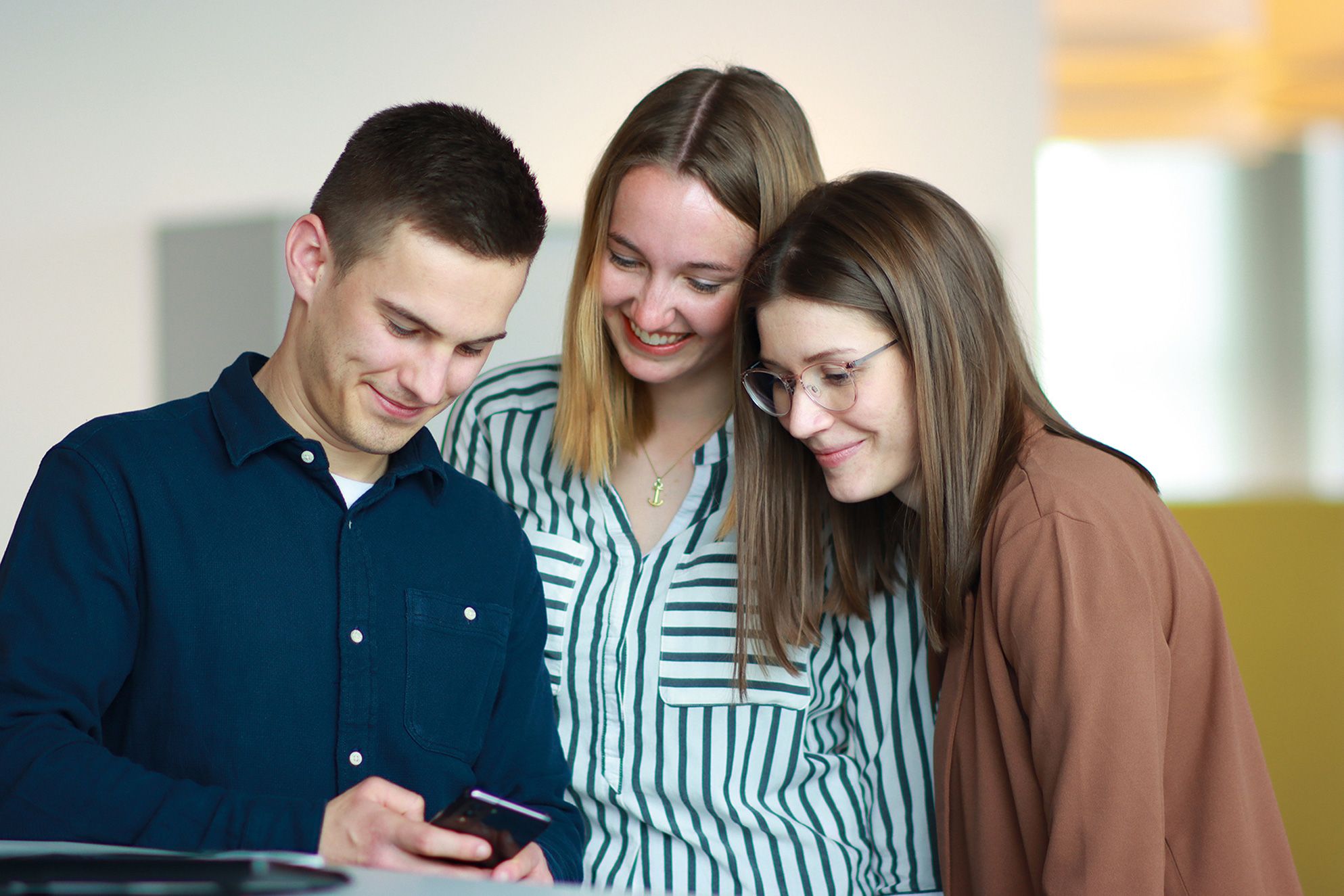 Three apprentices are spending time together laughing about something funny on a smartphone.