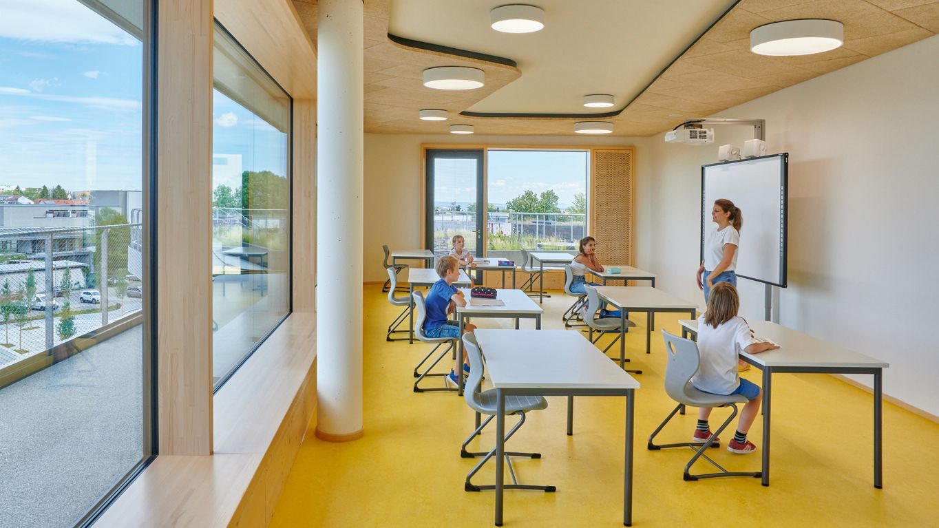 Des élèves de l'école Gotthard-Müller sont assis sur des chaises scolaires PantoSwing-LuPo à des tables d'école EcoTable et écoutent la professeure qui enseigne devant un tableau blanc interactif de VS.