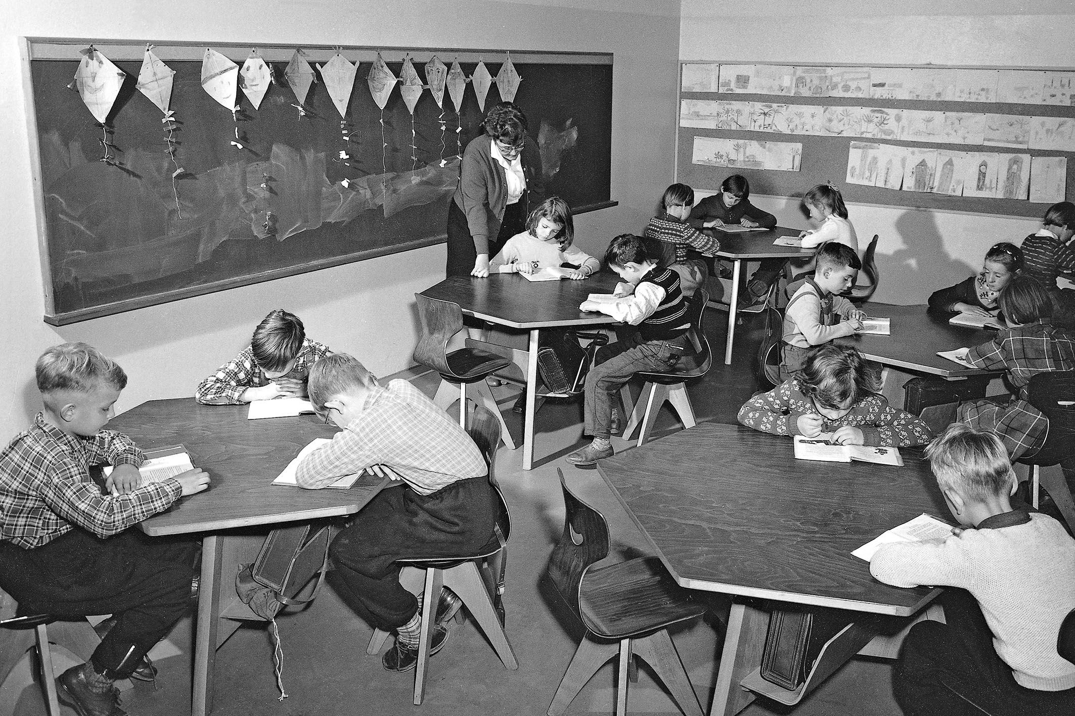 Black and white image of a classroom with group tables at which children are working.