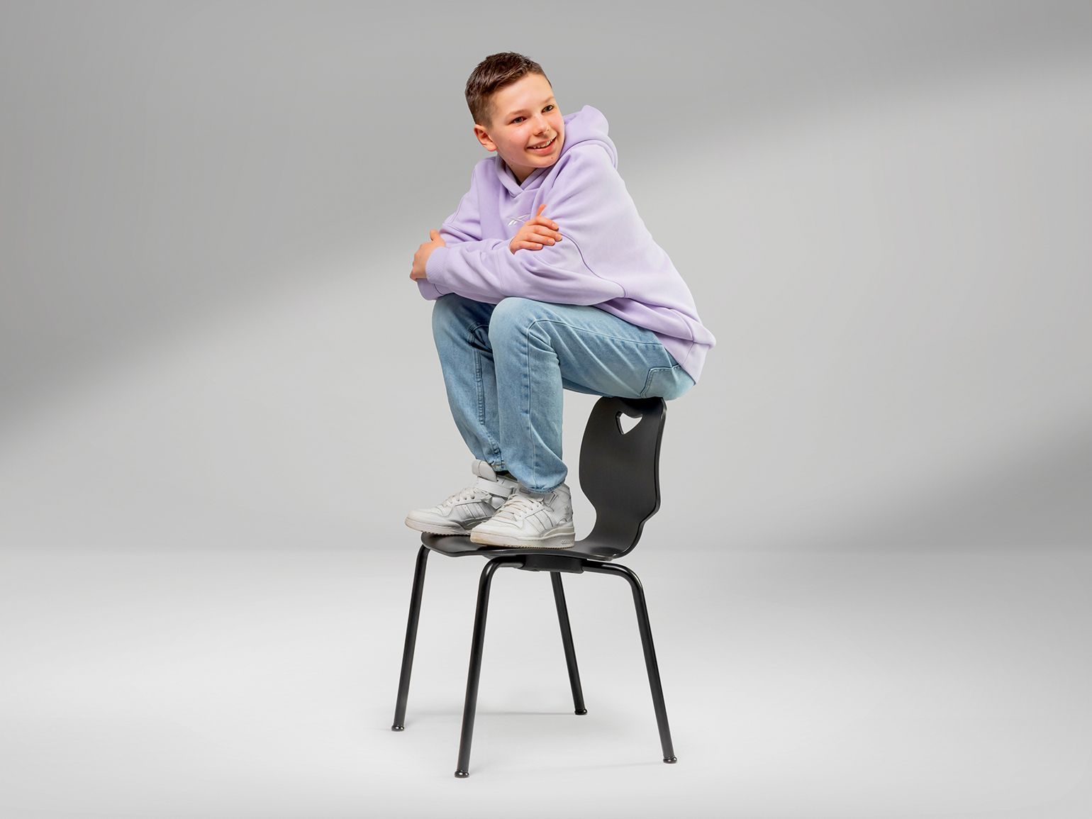 A boy is sitting on the backrest of a JUMPER Ply Four wooden chair by VS