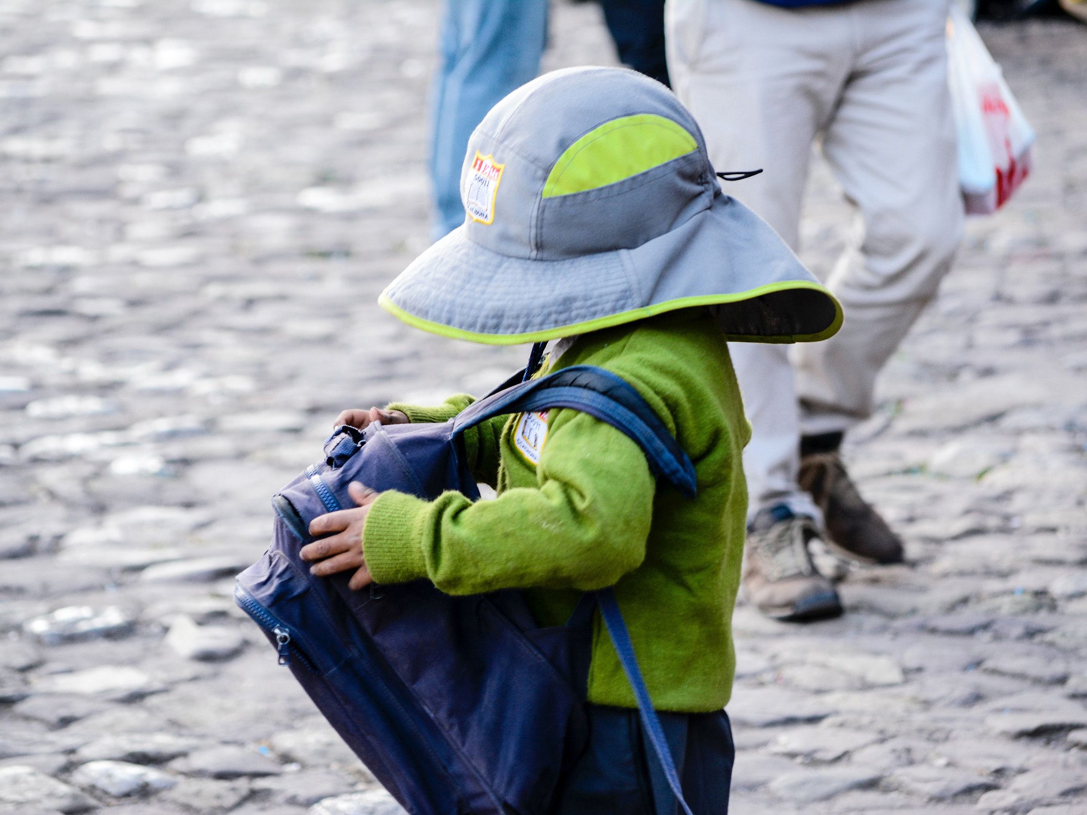 Une photo d'un jeune enfant avec un cartable portant un chapeau.