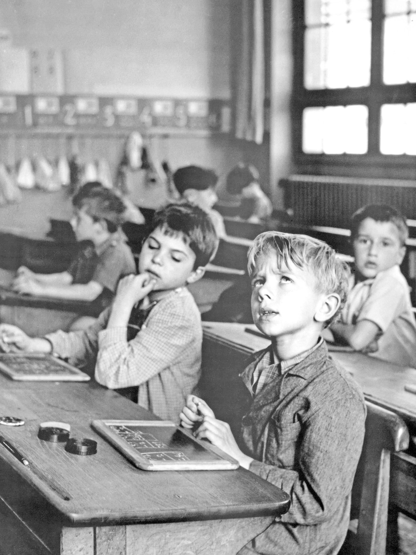 Black and white image of two boys sitting at a school desk and thinking