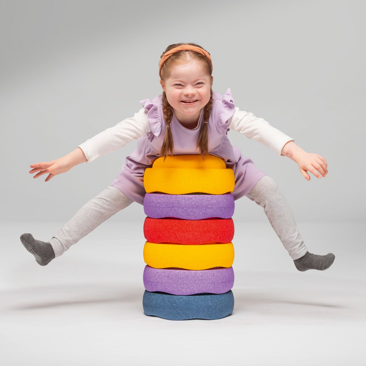 A girl is lying on her stomach on a stack of Stapelstein stones from the FloorFriends series by VS