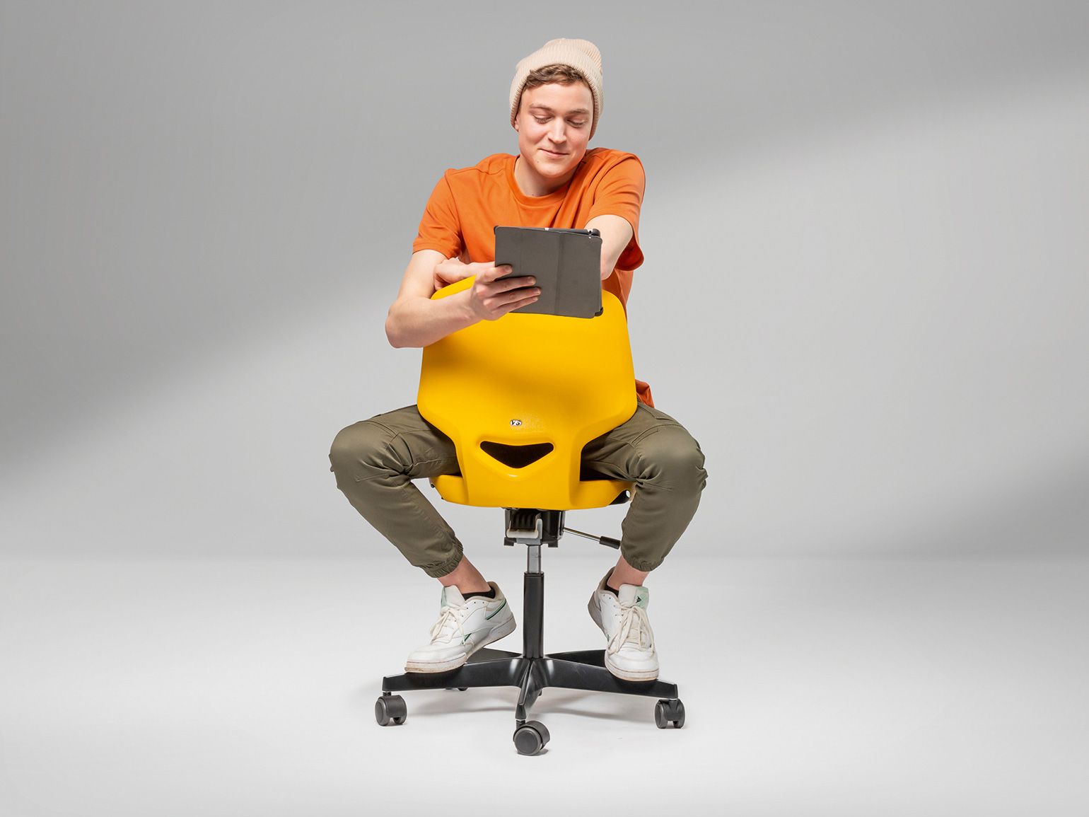 A young man sits astride a yellow JUMPER Air swivel chair by VS and looks at a tablet