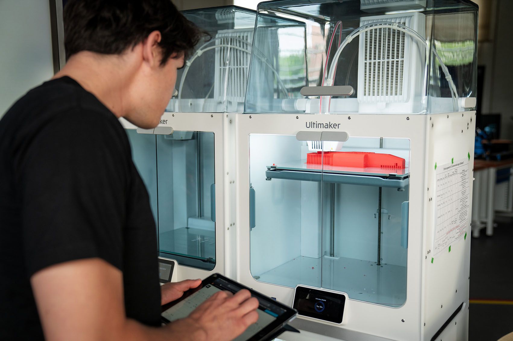 Young man holding a tablet operates a 3D printer.