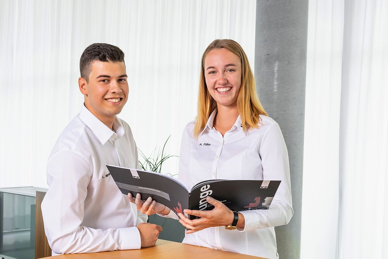 Two industrial business managers hold a VS catalogue in their hands and smile at the camera.