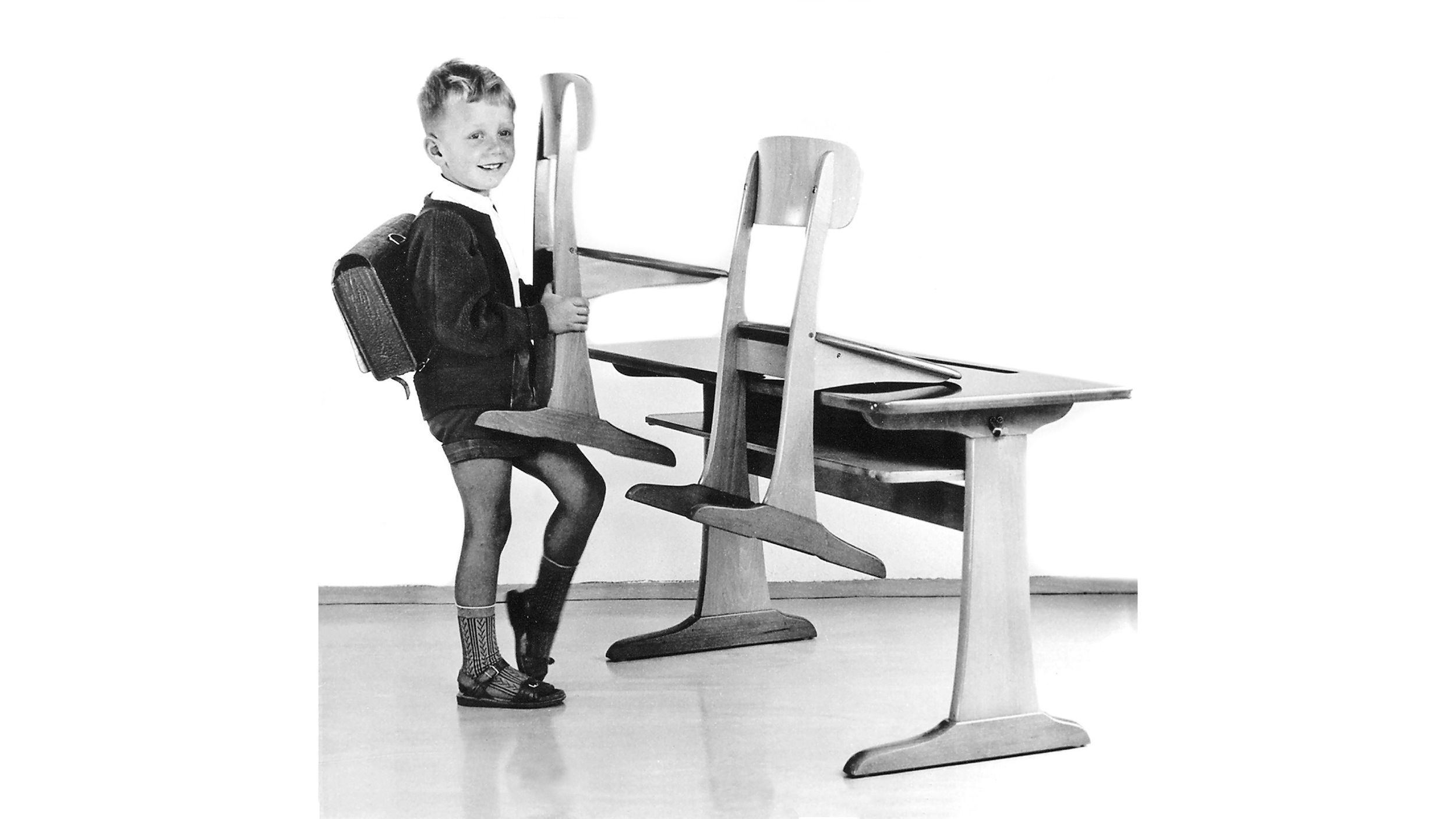 Schwarz-Weiß-Bild von einem Jungen, der einen VS Kufenstuhl aus Holz auf einen Kufentisch aufstuhlt.