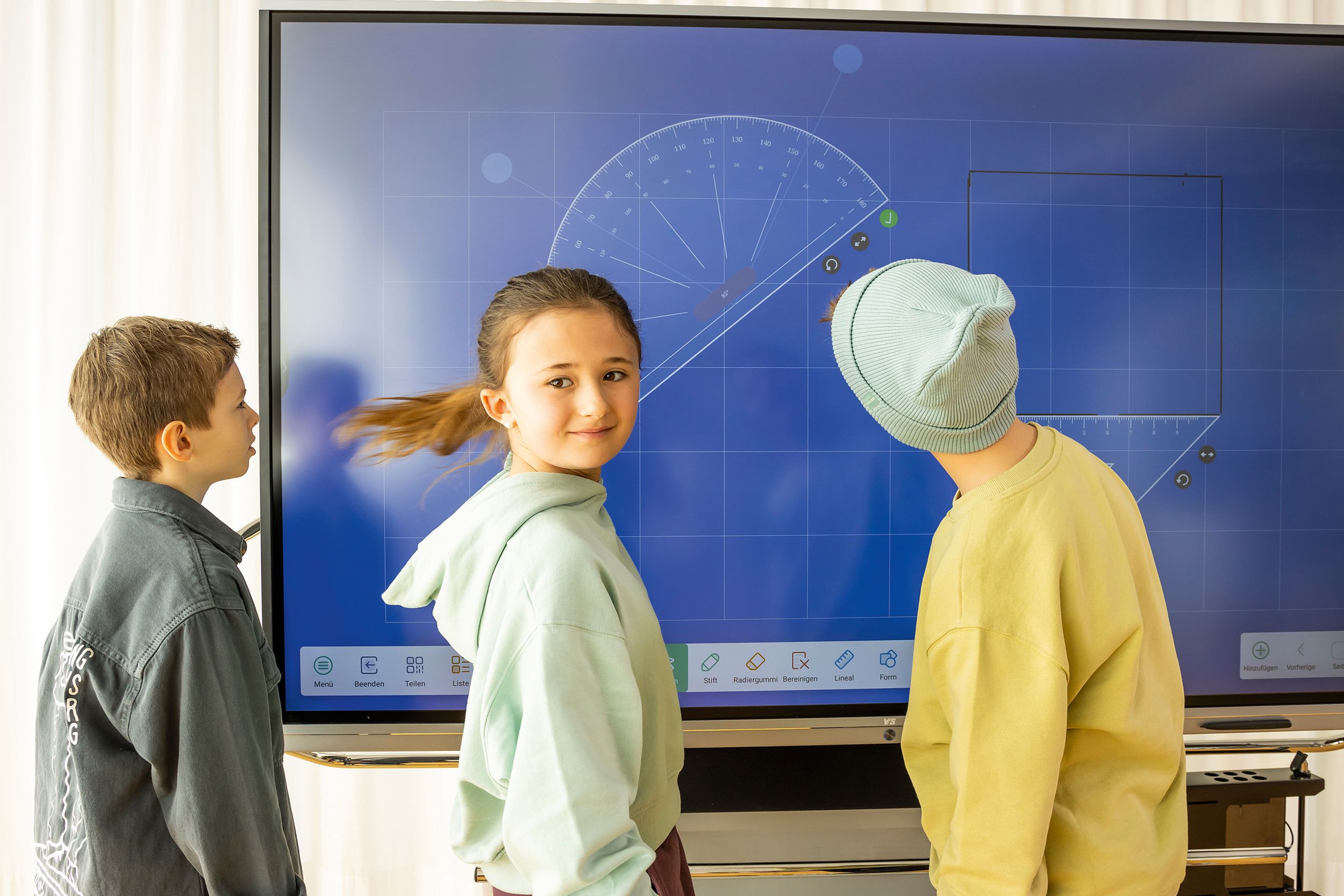 Trois enfants dessinent des formes géométriques sur un tableau blanc interactif de VS