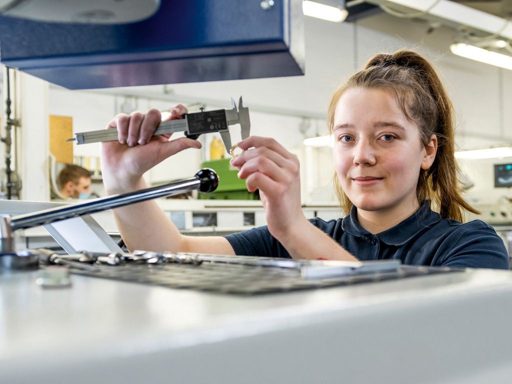 A VS apprentice in industrial mechanics measures the dimensions of a small part with a calliper.