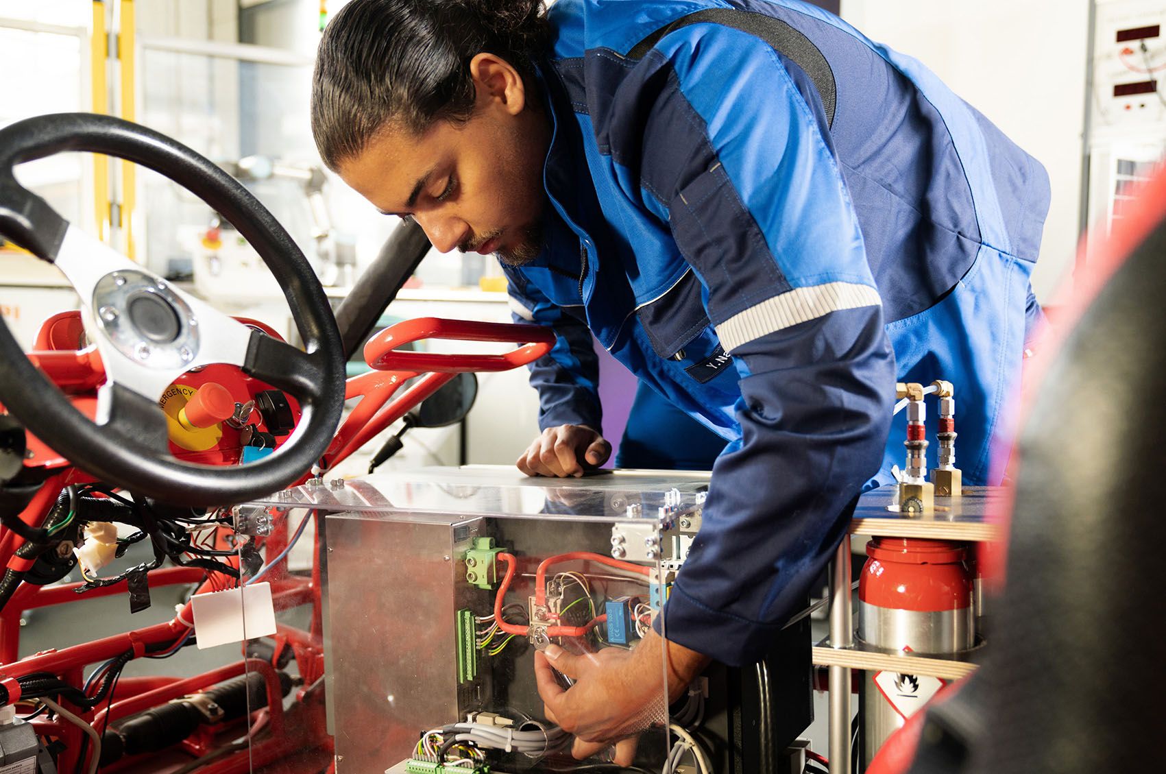 An apprentice works with a spanner on the electronics of a machine.