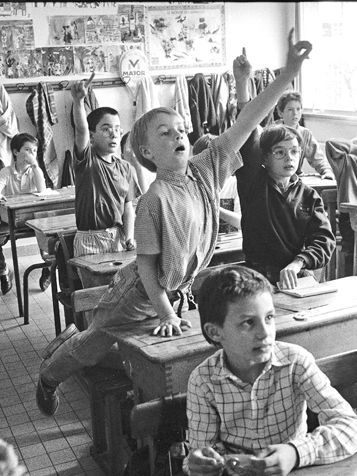 Eine Schwarz-Weiß-Aufnahme aus einem Klassenzimmer mit Fokus auf einen Jungen, der sich motiviert meldet