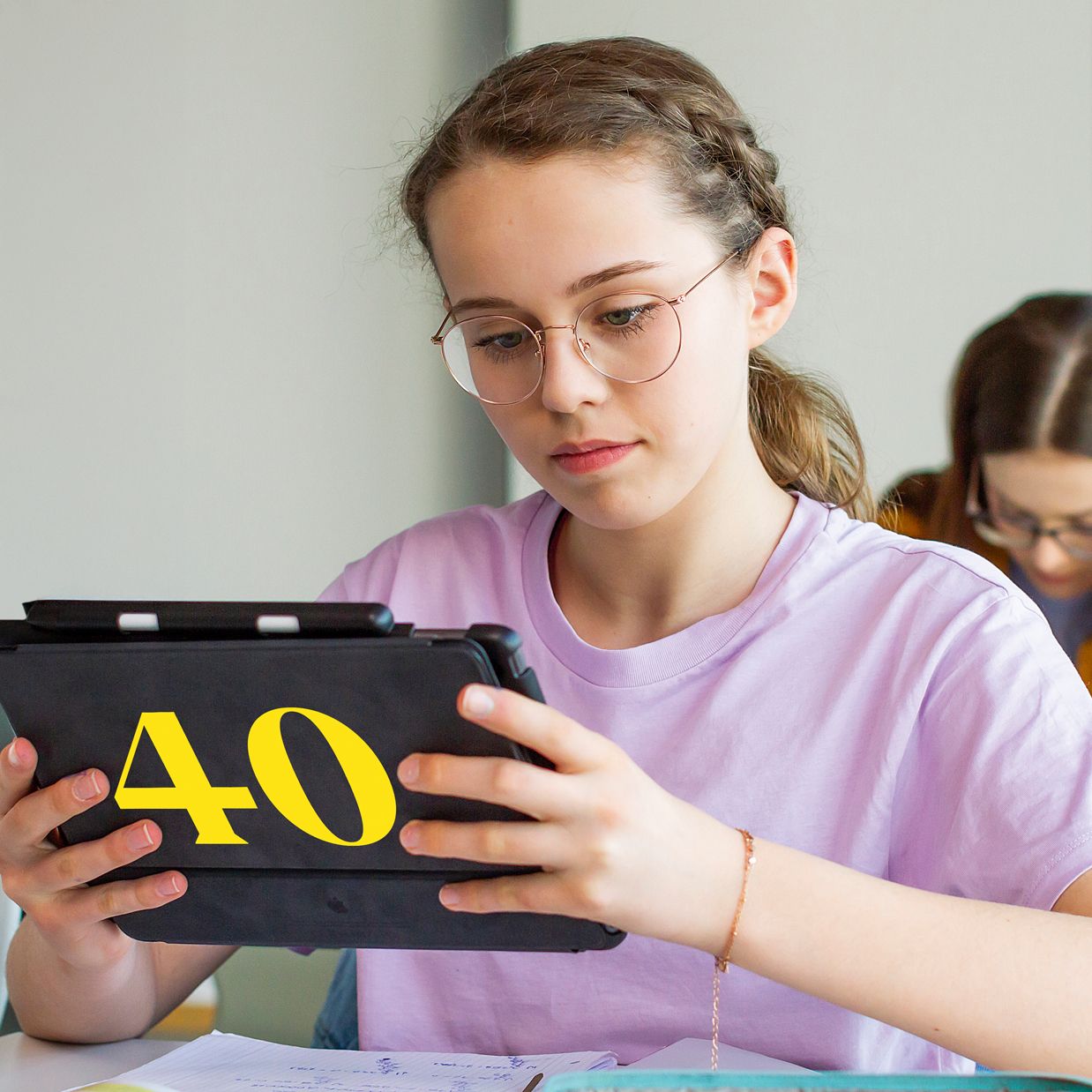 Une fille assise à une table, utilisant une tablette numérique pour naviguer ou travailler