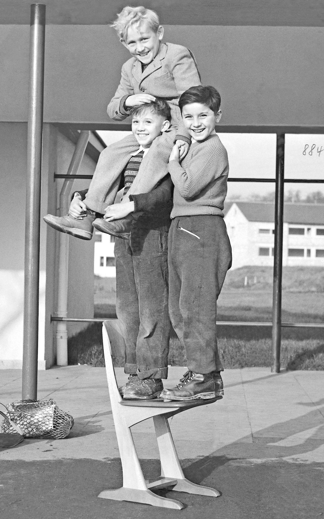 Black and white image taken 1950 of three children standing all together on a wooden skid chair by VS.