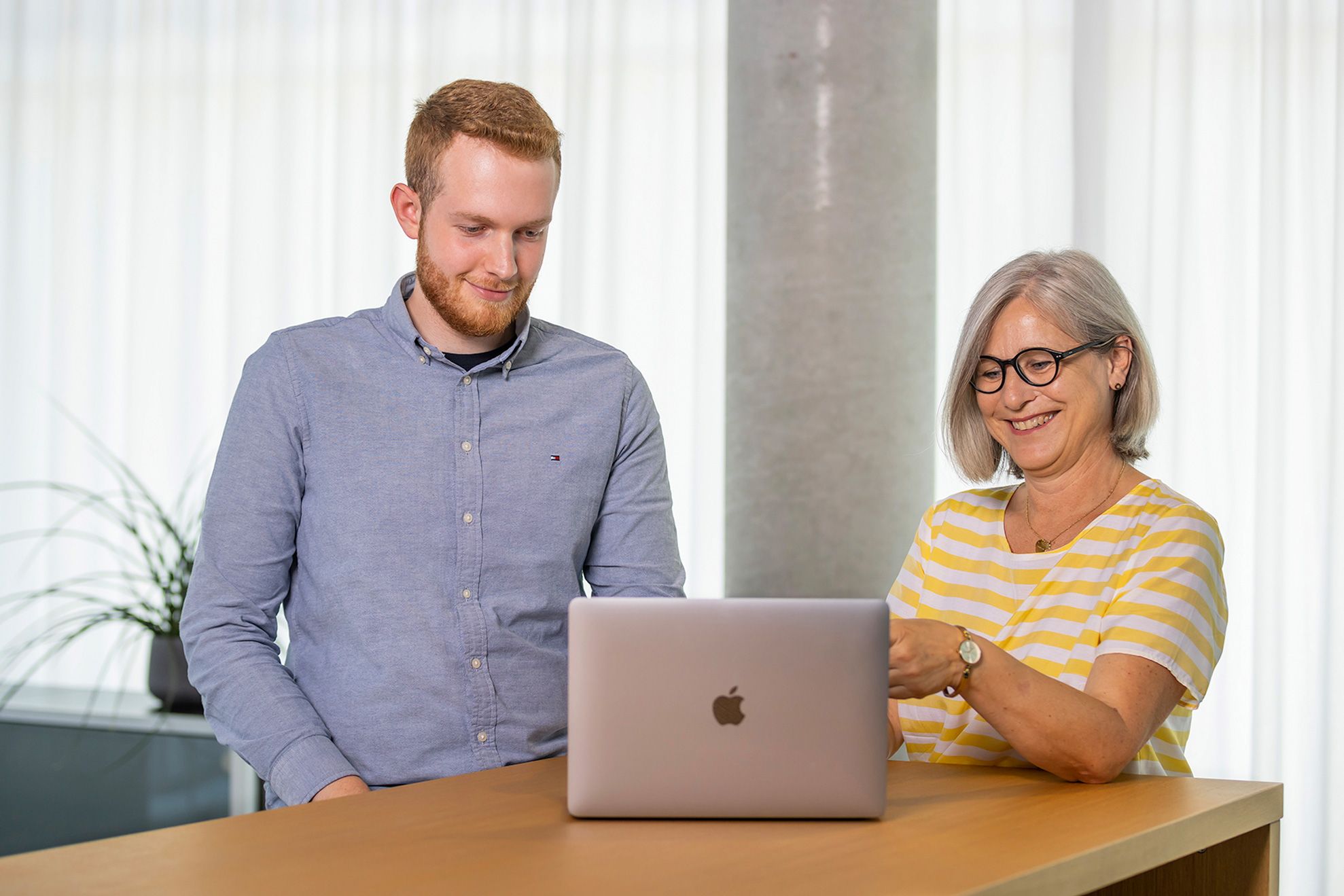 Two people are standing at a cheek table looking at a laptop