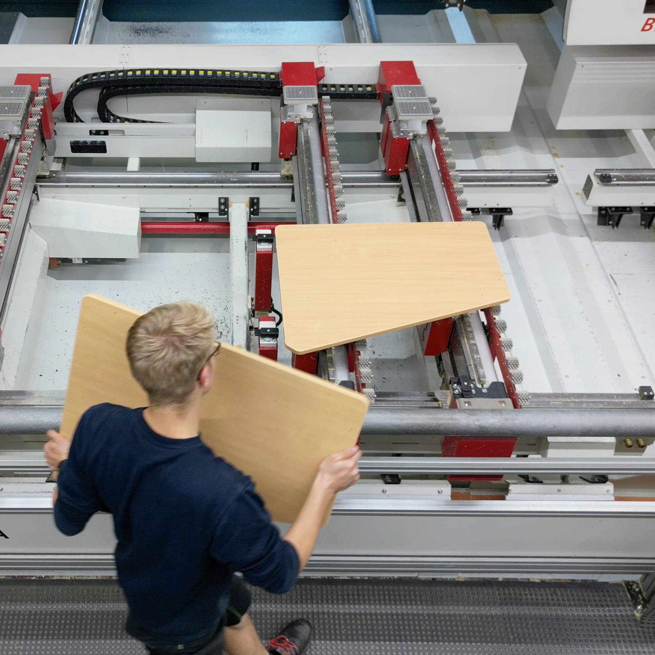 An employee carries a table top of the asymmetrical Tano table next to a production machine