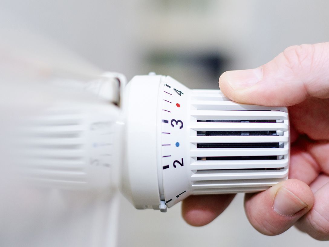 Hand stellt Thermostat einer Heizung ein um Energie zu sparen