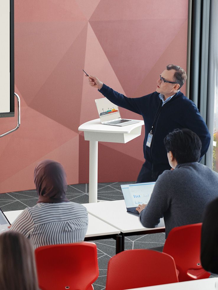 A speaker points at a statistic on a digital whiteboard in a seminar room furnished by VS