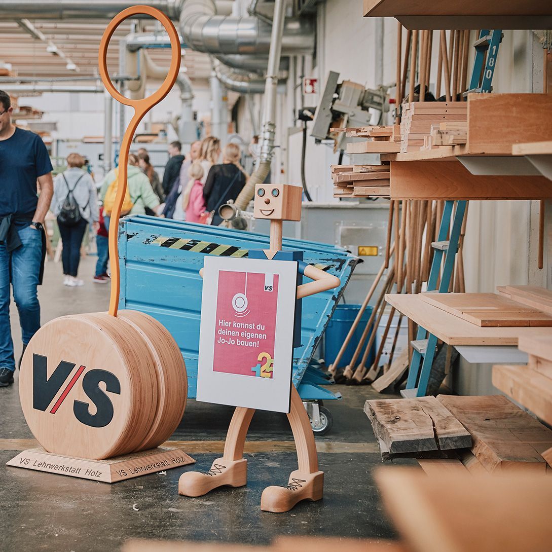 Ein Holzaufsteller lädt Besucher des Tags der offenen Tür von VS ein, einen Jo-Jo in der Lehrwerkstatt bauen können